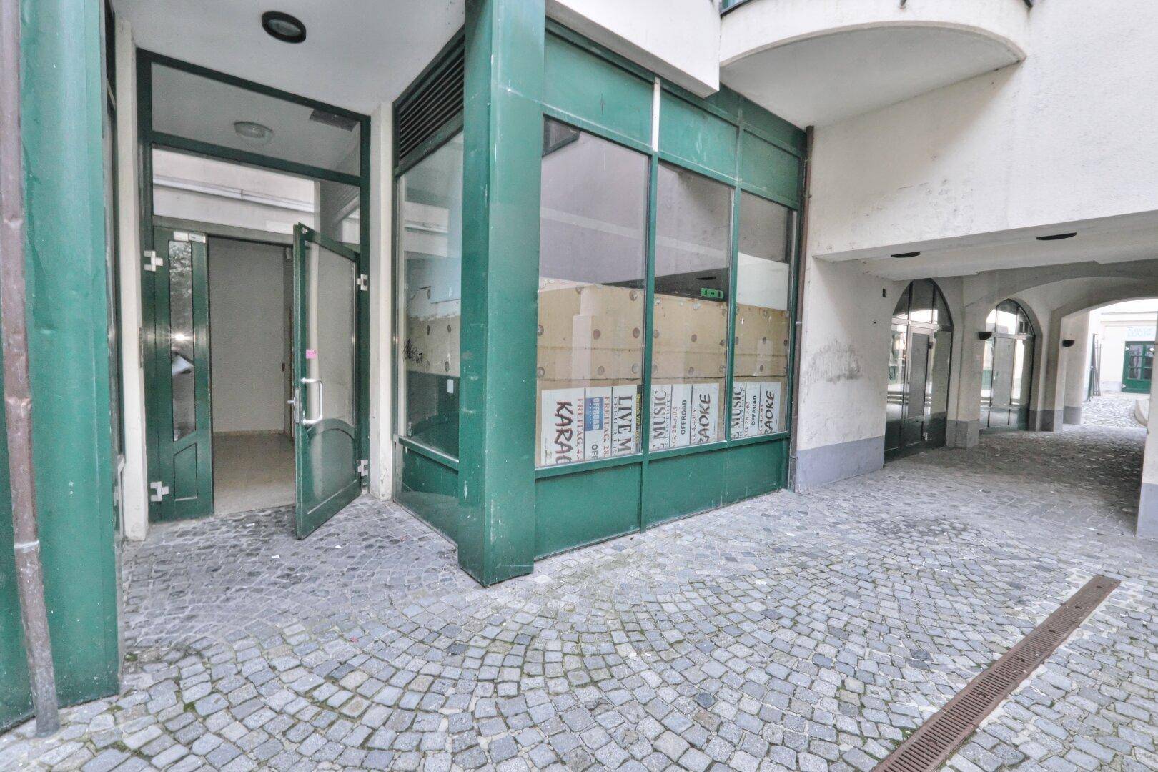Eingang zu einer Gewerbeeinheit im Innenhof mit großen Glasfronten und Kopfsteinpflaster.