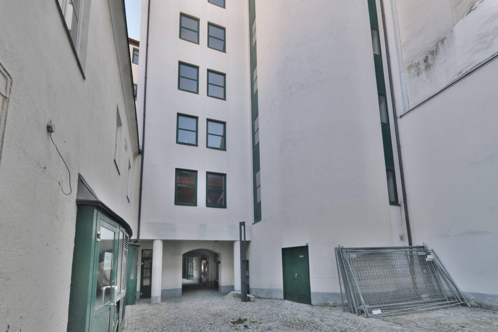 Innenhof mit Kopfsteinpflaster und einem hohen Gebäude, das von weiteren Gebäuden umgeben ist.