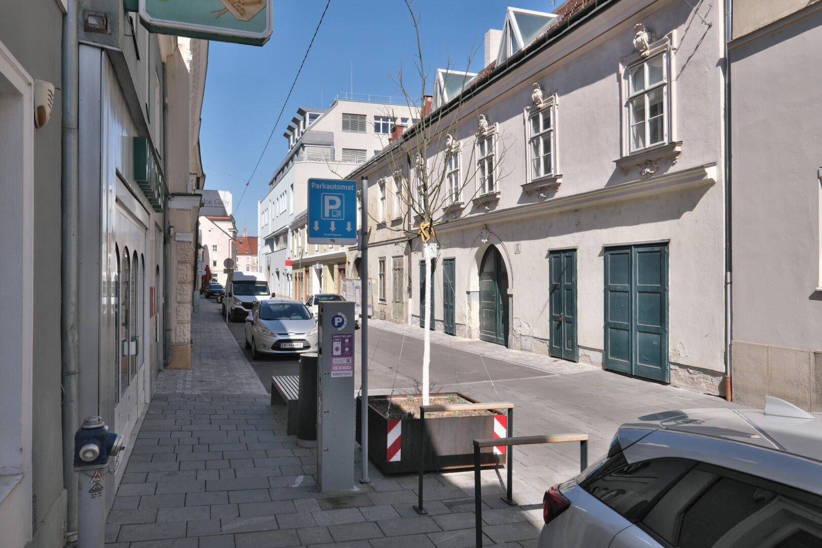 Straße mit parkenden Autos und historischen Gebäuden, die eine angenehme städtische Atmosphäre schaffen.