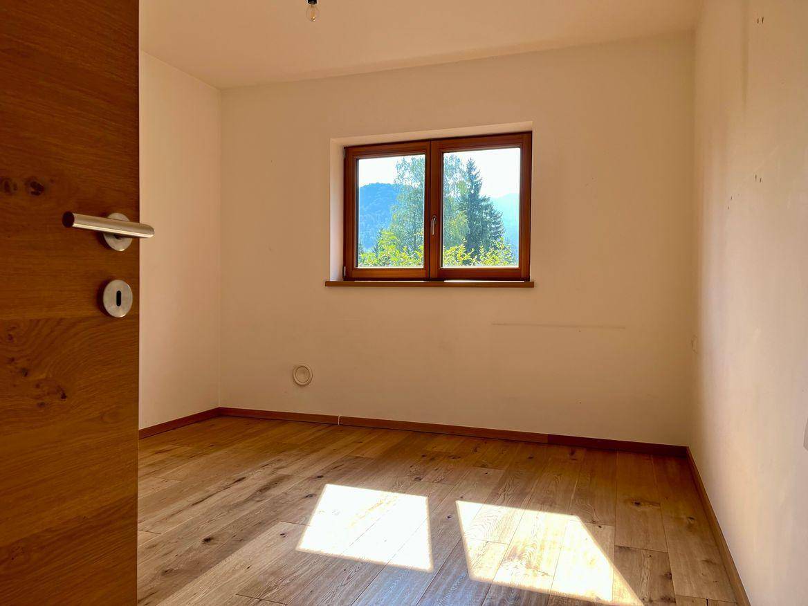 Helles Schlafzimmer mit Holzboden und Fenster, das einen schönen Blick auf die Berge bietet.
