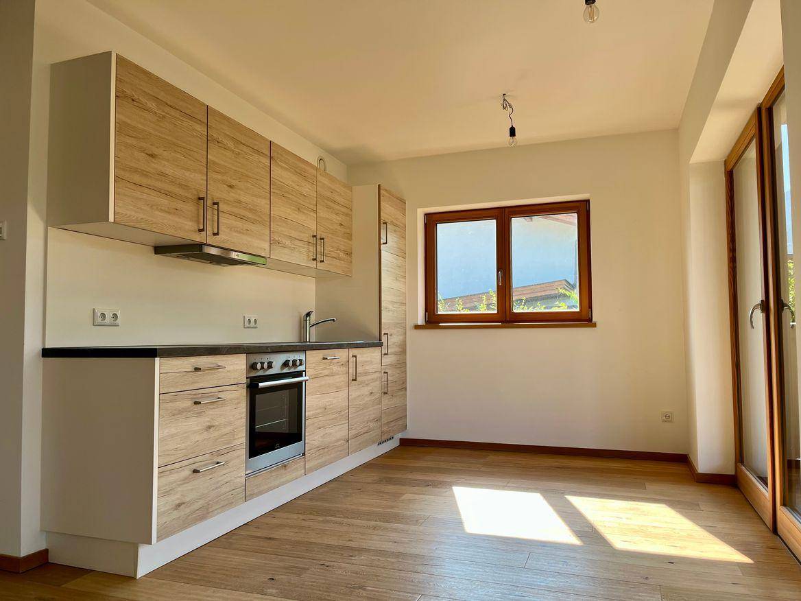 Moderne Einbauküche mit hellen Holzfronten, dunkler Arbeitsplatte und Fenster mit Ausblick.