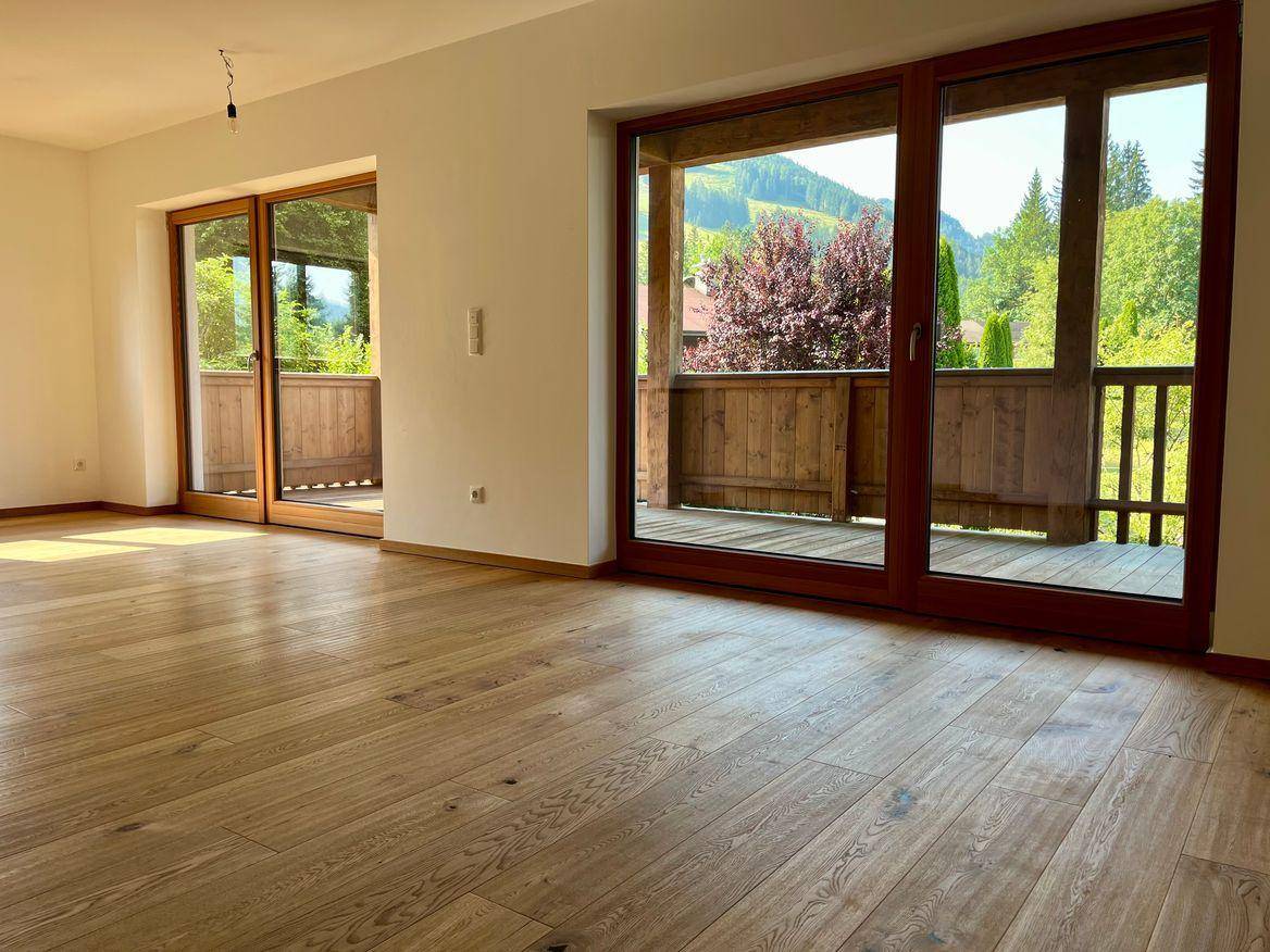 Lichtdurchfluteter Wohnbereich mit Holzboden und großen Schiebetüren zur Terrasse mit Bergblick.