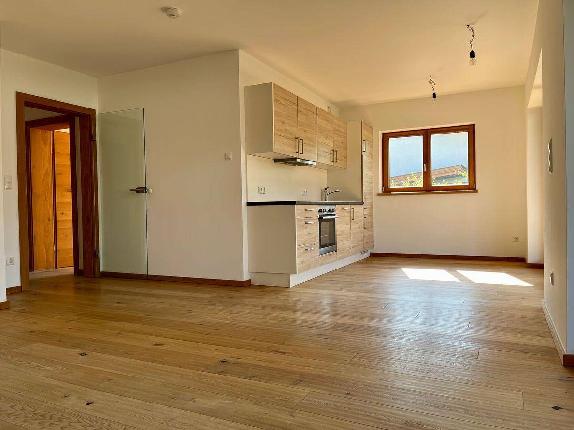 Heller offener Wohnbereich mit neuer Einbauküche, Holzboden und viel Tageslicht.