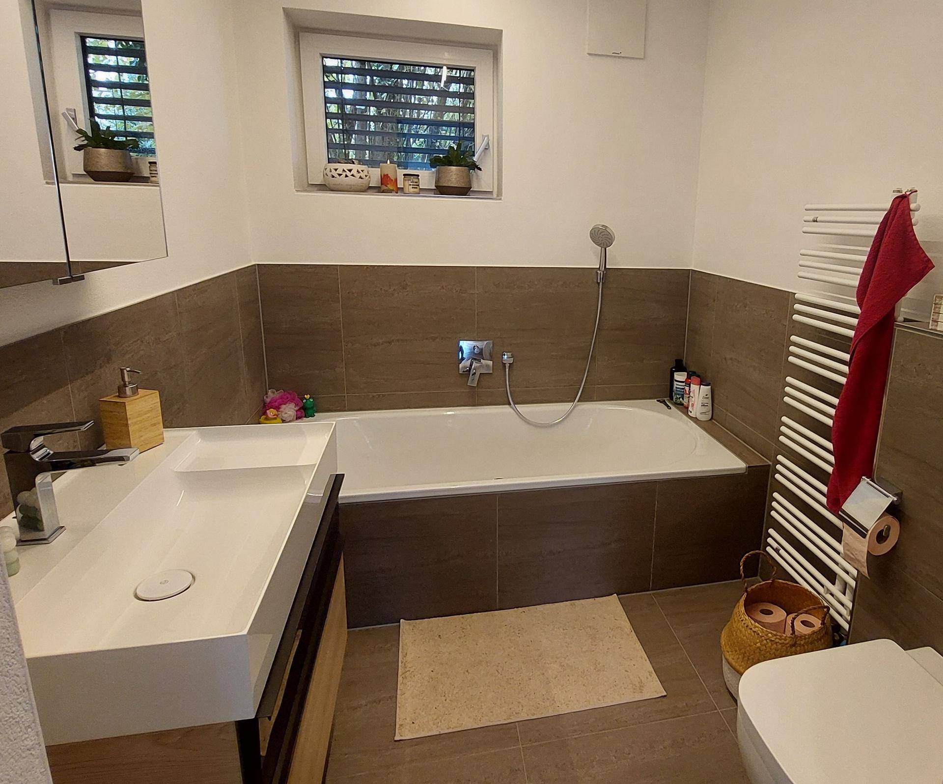 Modernes Badezimmer mit Badewanne, Einzelwaschbecken und beheiztem Handtuchhalter, mit Fenster.
