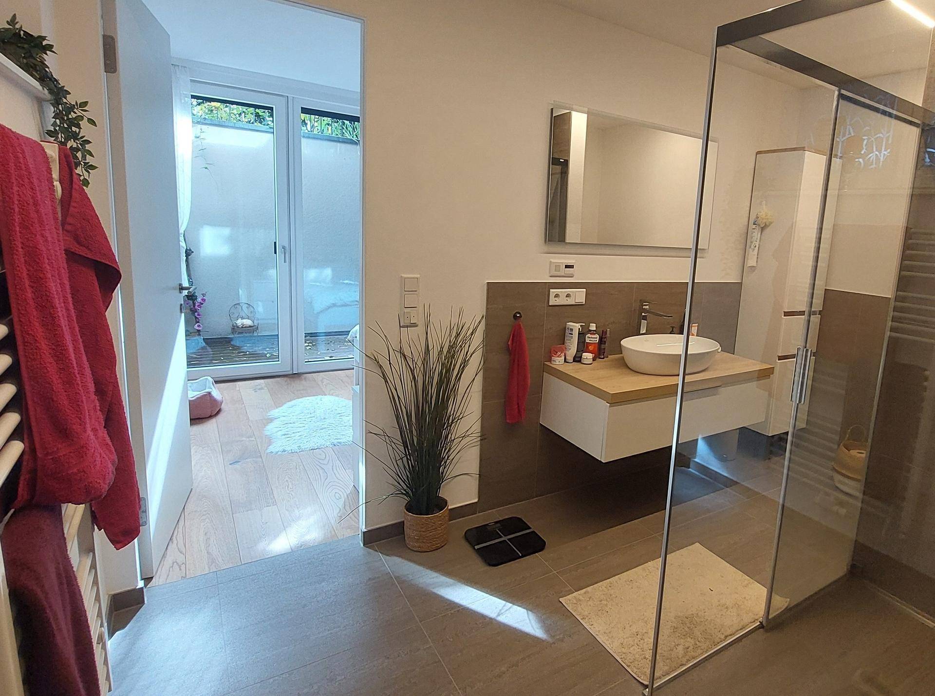 Helles Badezimmer mit begehbarer Dusche und Zugang zu einem Außenbereich, modern gefliest.
