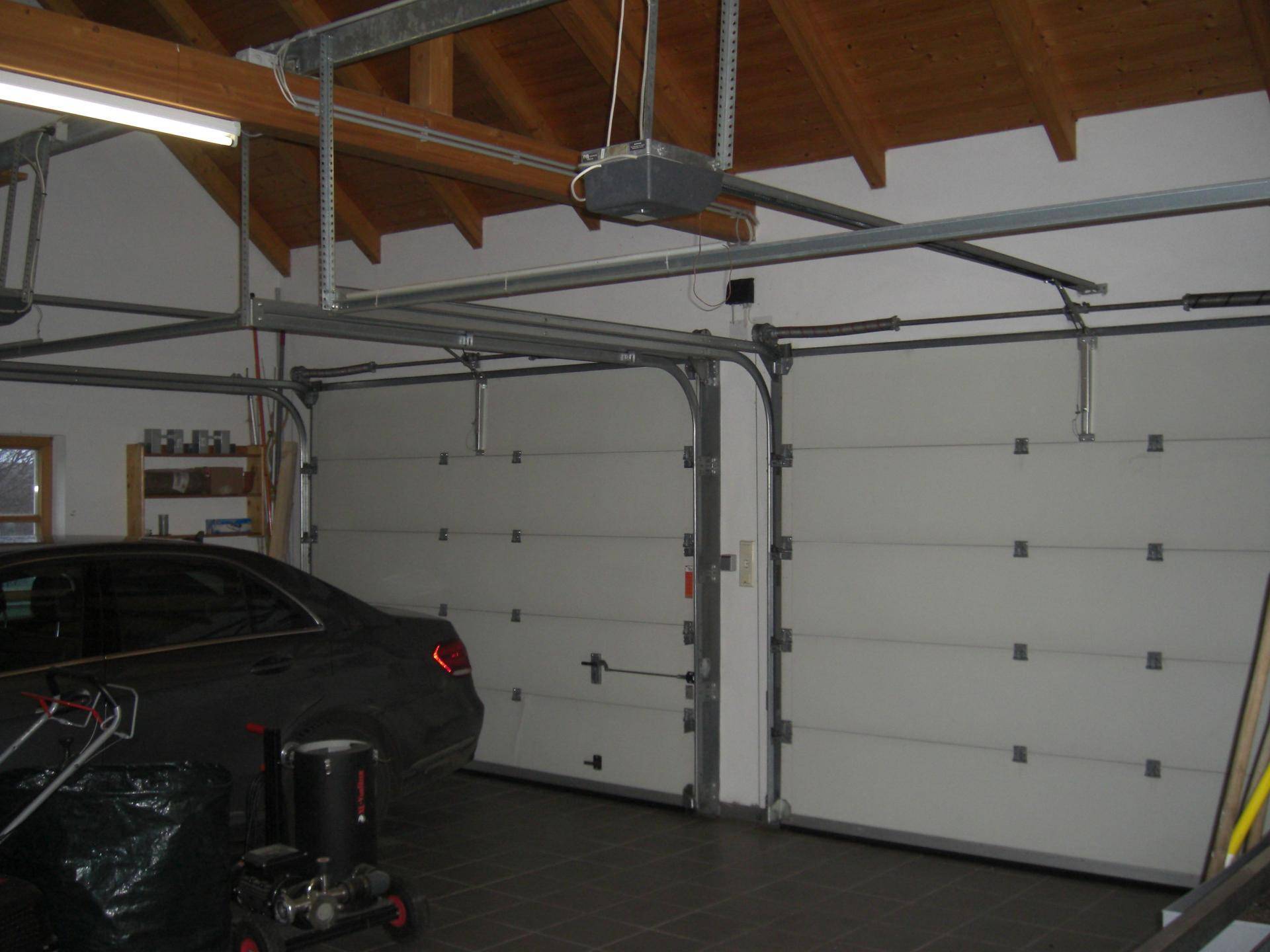 Geräumige Doppelgarage mit zwei Sektionaltoren, Fliesenboden und sichtbarer Holzkonstruktion des Daches.