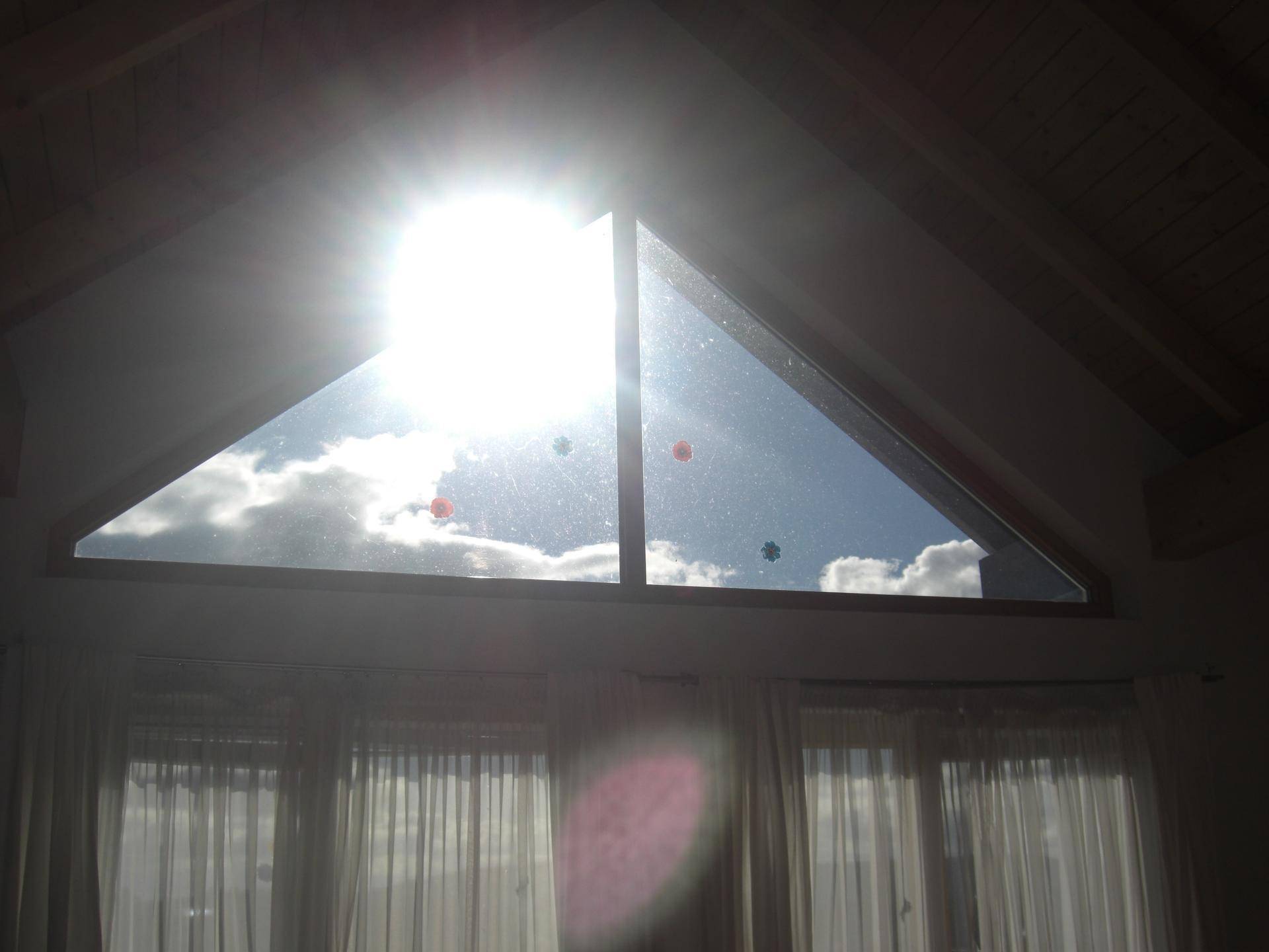 Helles Giebelfenster im Dachgeschoss, das viel Sonnenlicht und einen weiten Blick auf den bewölkten Himmel bietet.