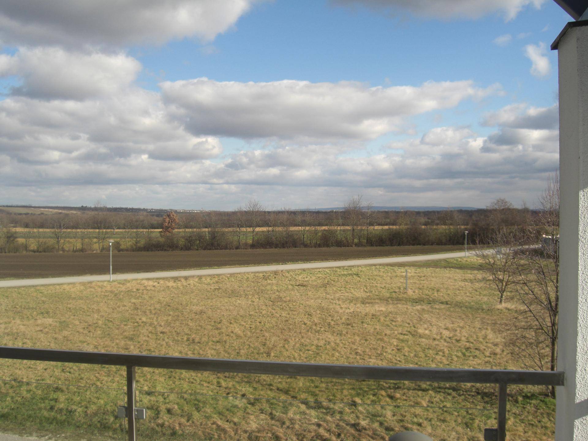 Weitläufiger Blick von einem Balkon über Felder und die ländliche Umgebung unter einem bewölkten Himmel.