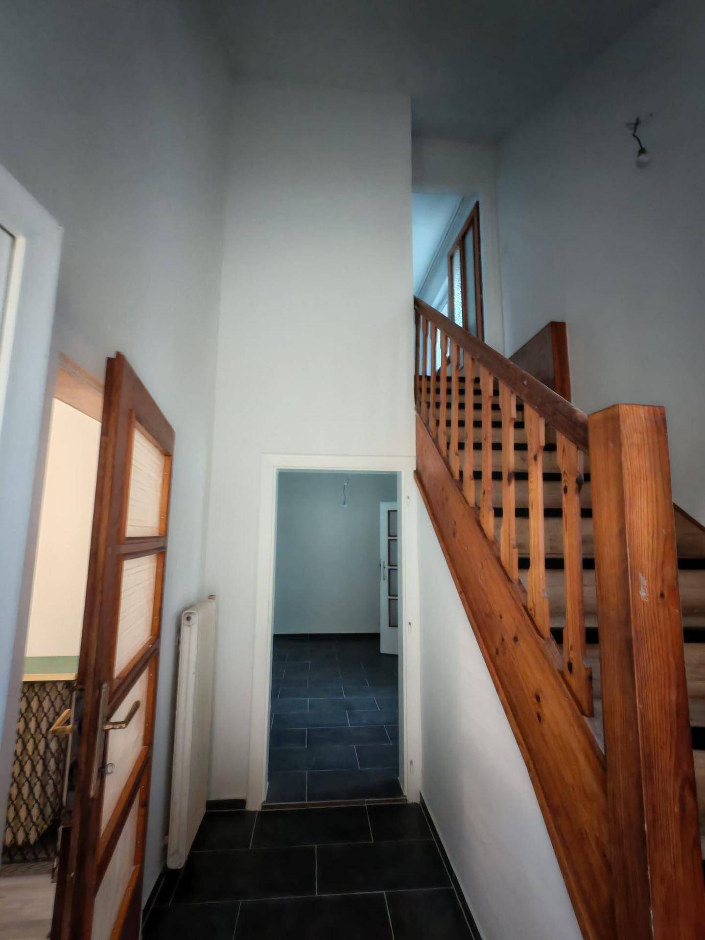 Heller Flur mit Holztreppe und dunklen Fliesen, der zu weiteren Räumen führt.