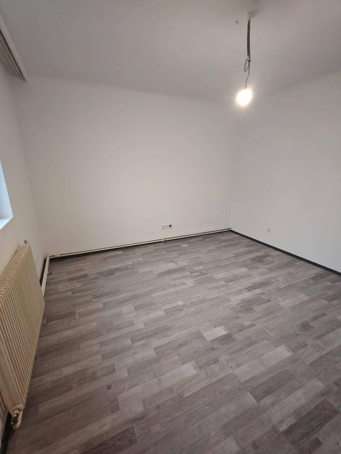 Leerer Raum mit hellem Laminatboden und weißen Wänden, bereit zur individuellen Gestaltung.