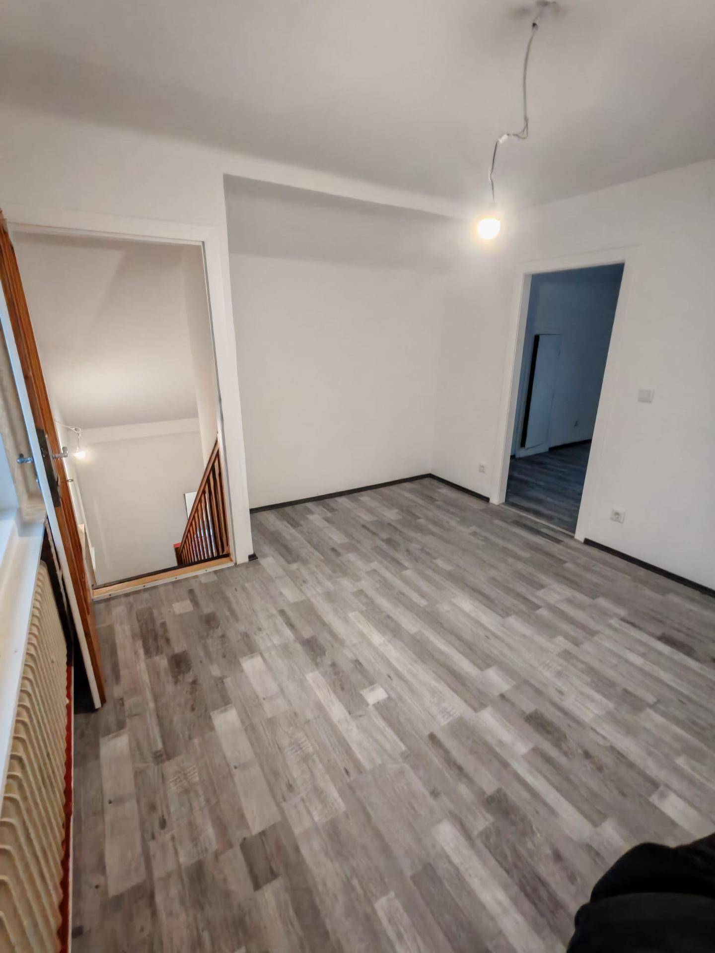 Heller Wohnraum mit Laminatboden und offenem Zugang zum Treppenhaus.