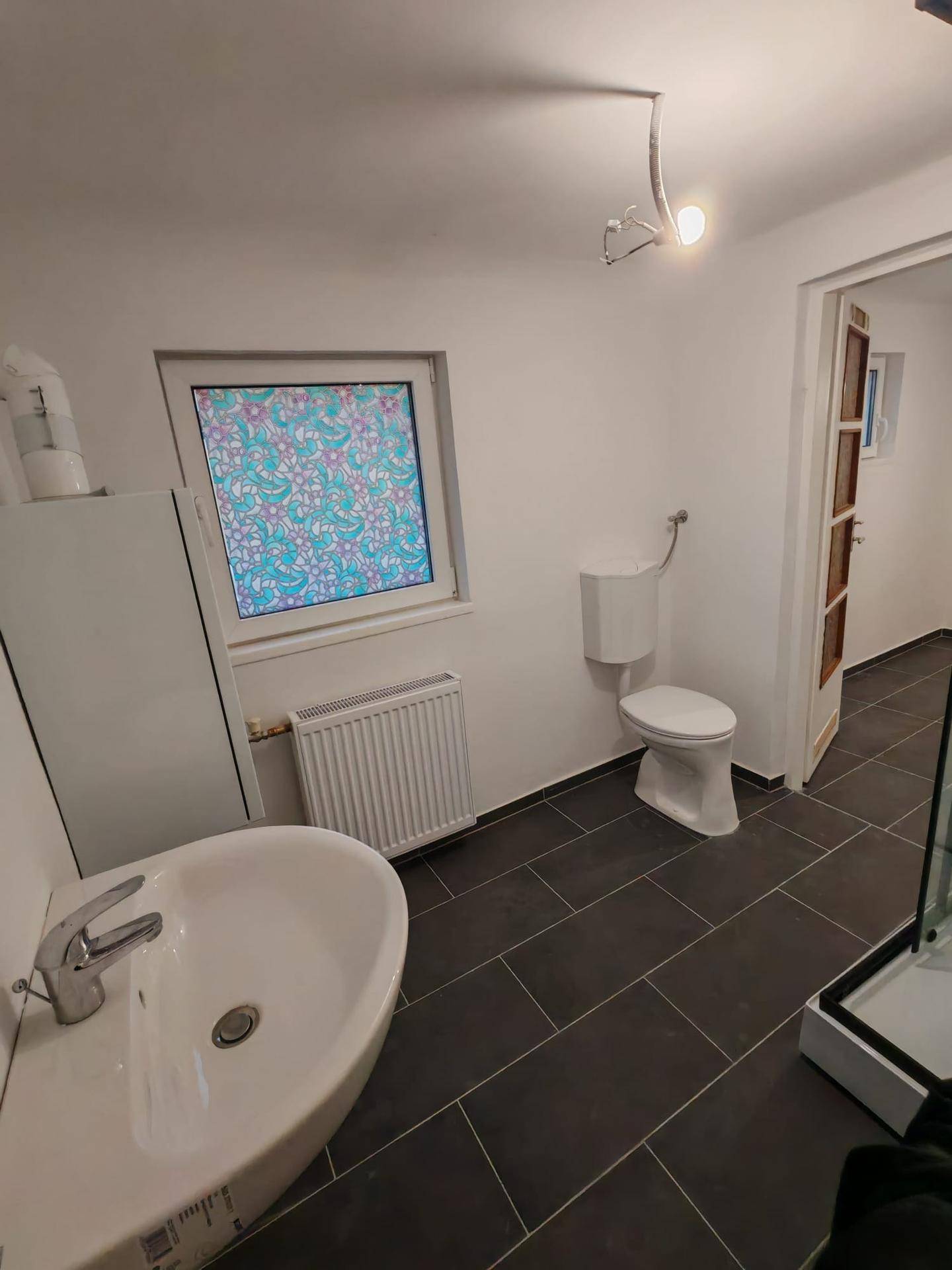 Helles Badezimmer mit Waschbecken, WC und Fenster mit dekorativer Folie.