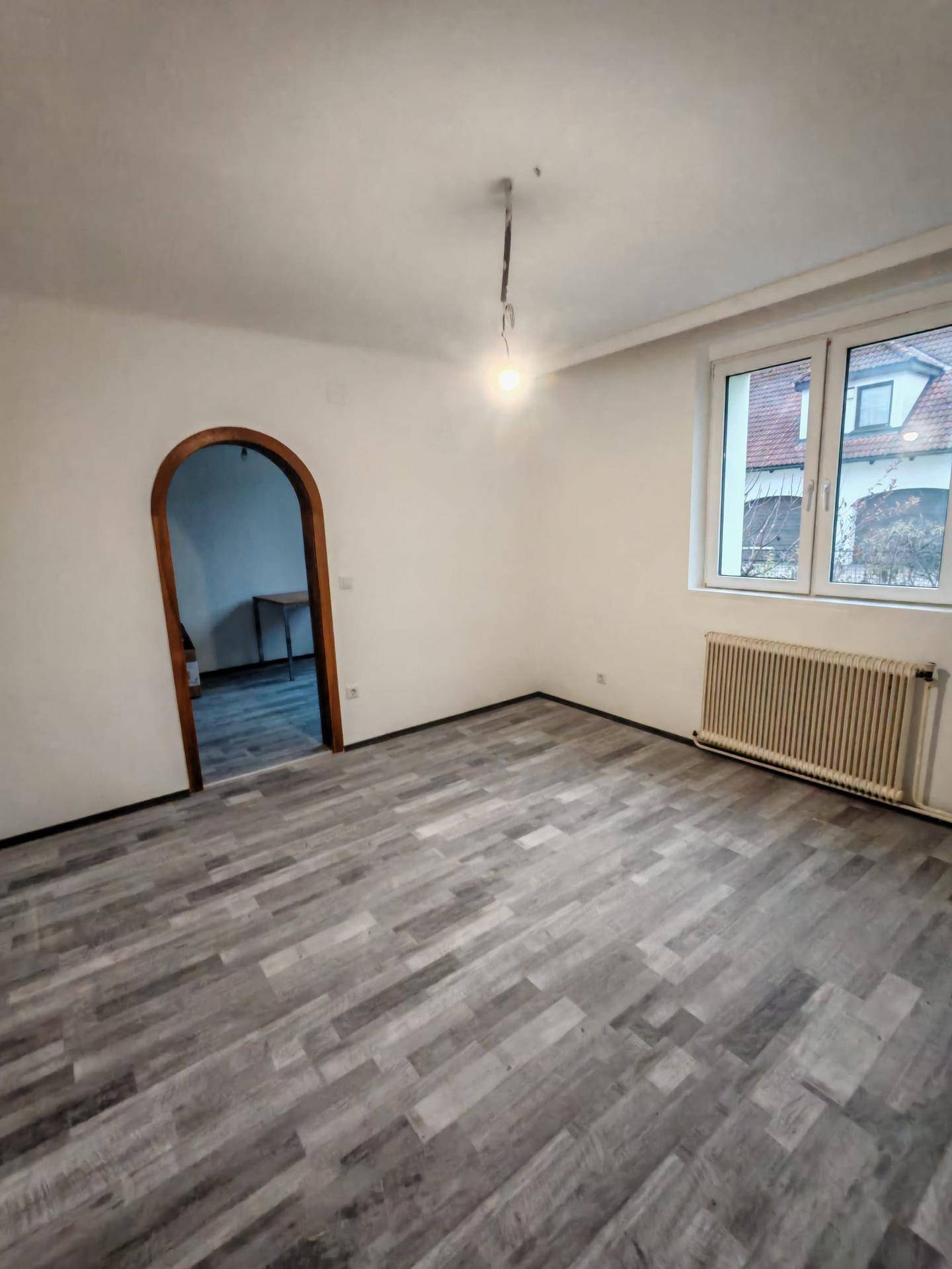 Helles Wohnzimmer mit Laminatboden, großem Fenster und einem Heizkörper darunter.