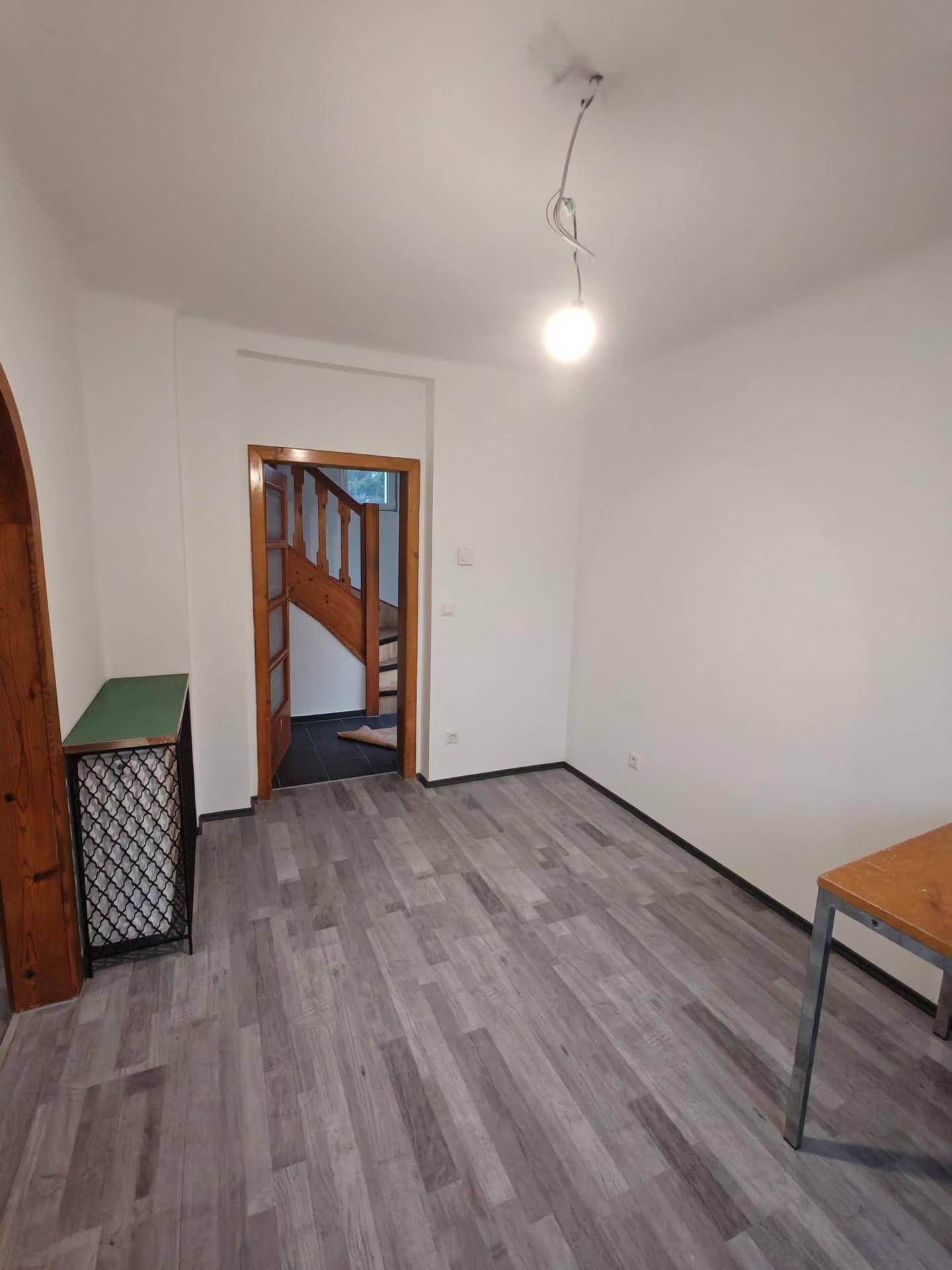 Geräumiges Zimmer mit Laminatboden und Blick auf den Flur mit Holztreppe.