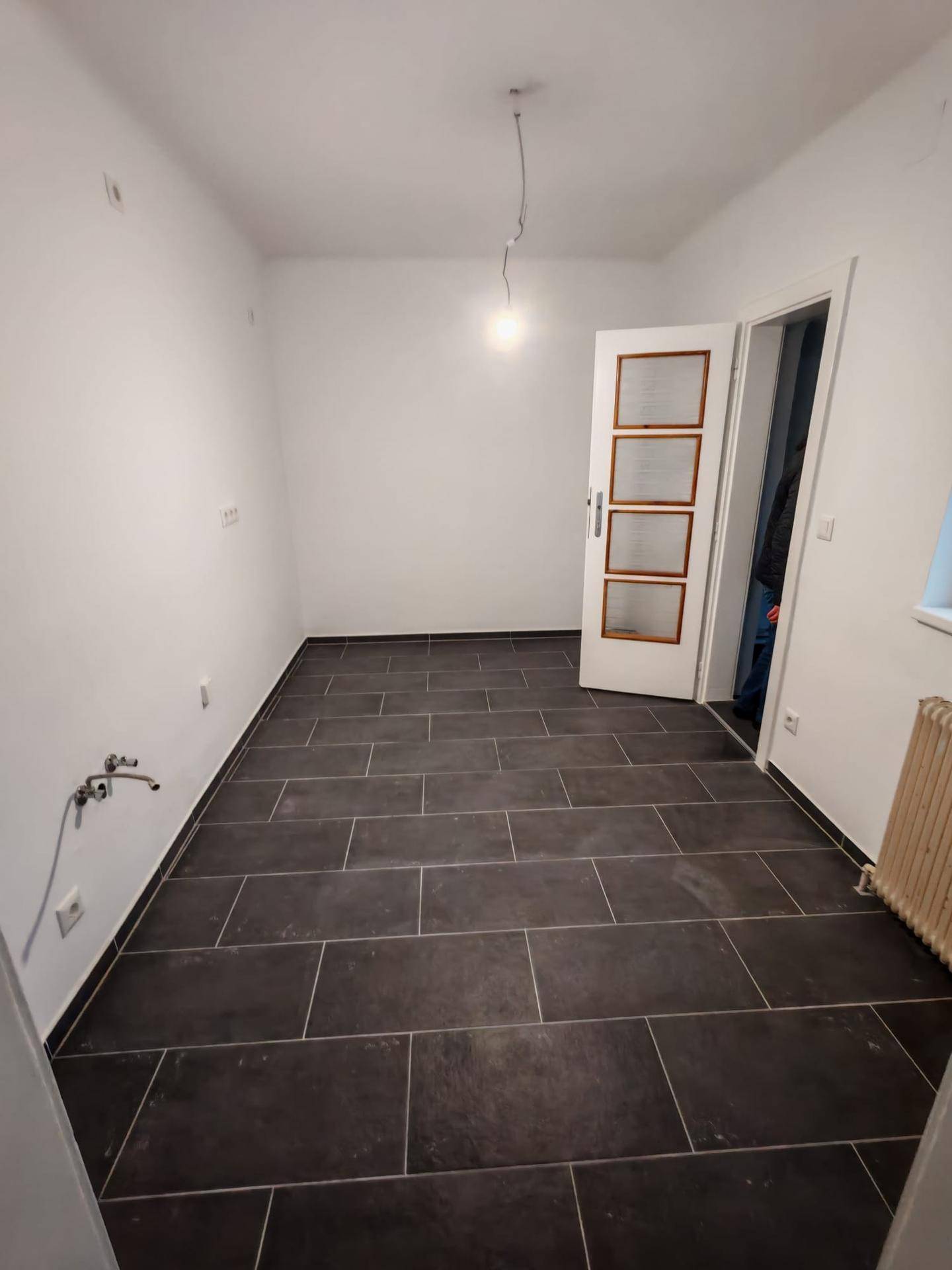 Leerer Küchenraum mit dunklen Fliesen und Anschlüssen für eine zukünftige Einbauküche.