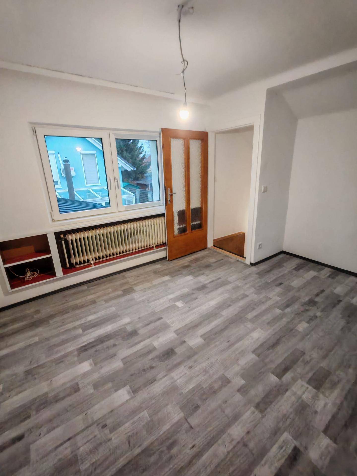 Geräumiges Zimmer mit Laminatboden, Fenster und Heizkörper unterhalb der Fensterbank.