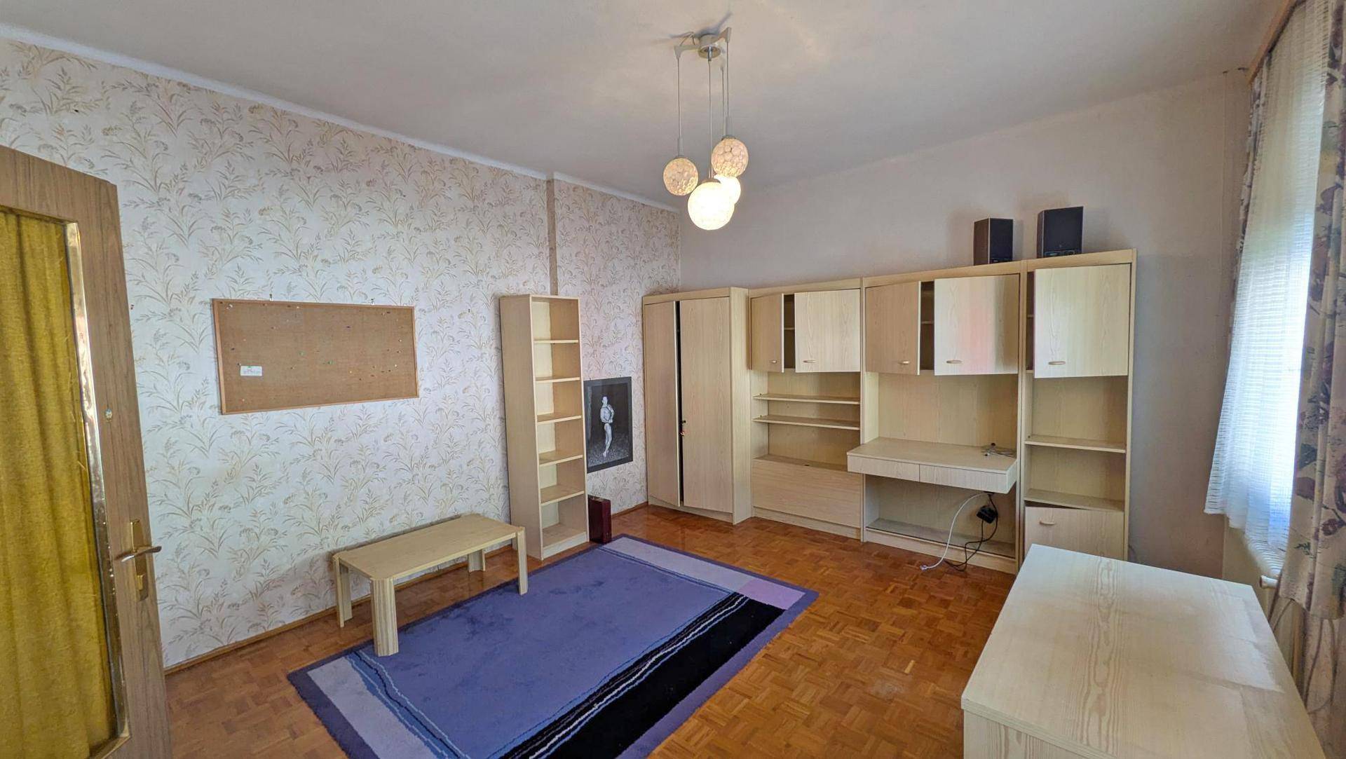 Funktional eingerichtetes Zimmer mit gemusterter Tapete und modularen Möbeln.