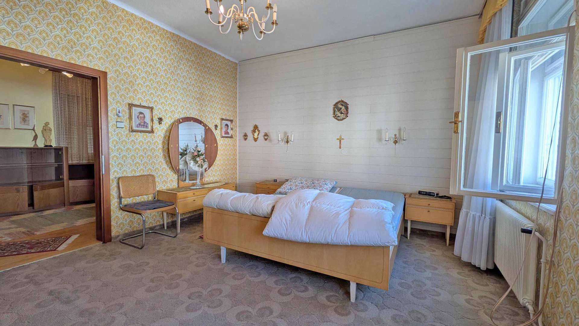 Gemütliches Schlafzimmer mit gemusterter Tapete, Einzelbett und traditionellen Holzmöbeln.