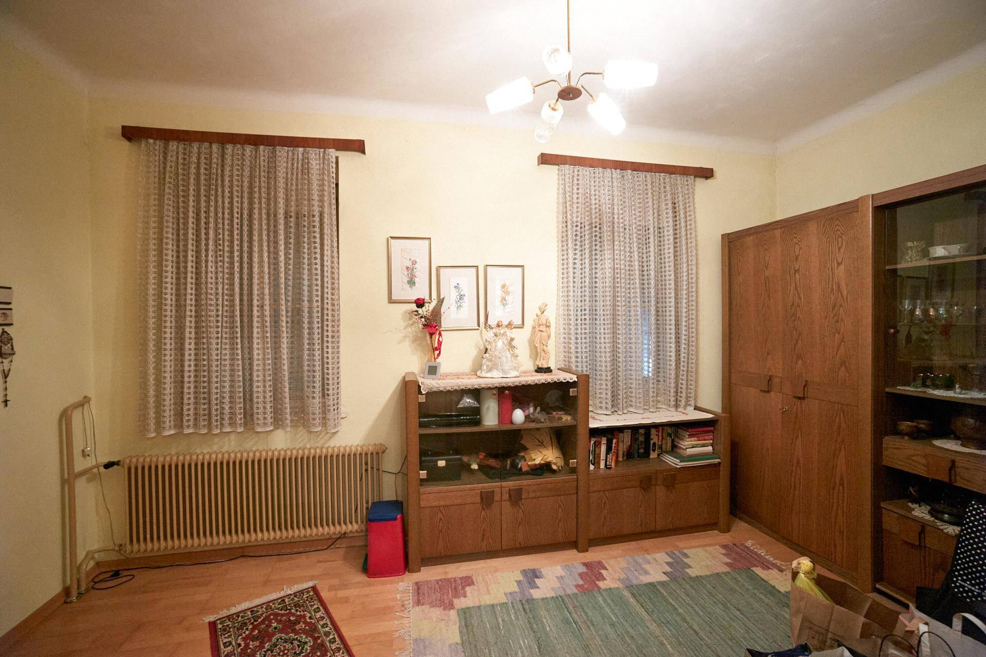 Helles Zimmer mit gelben Wänden, zwei Fenstern und traditionellen Holzmöbeln.