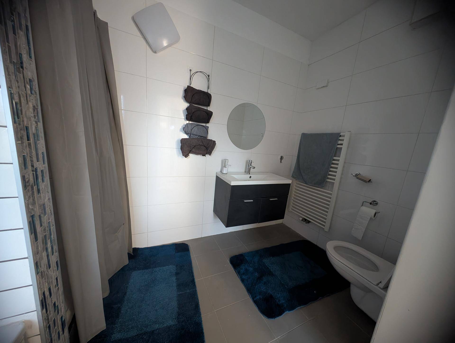 Modernes Badezimmer mit Dusche, Hänge-WC, beheiztem Handtuchhalter und grauem Fliesenboden.
