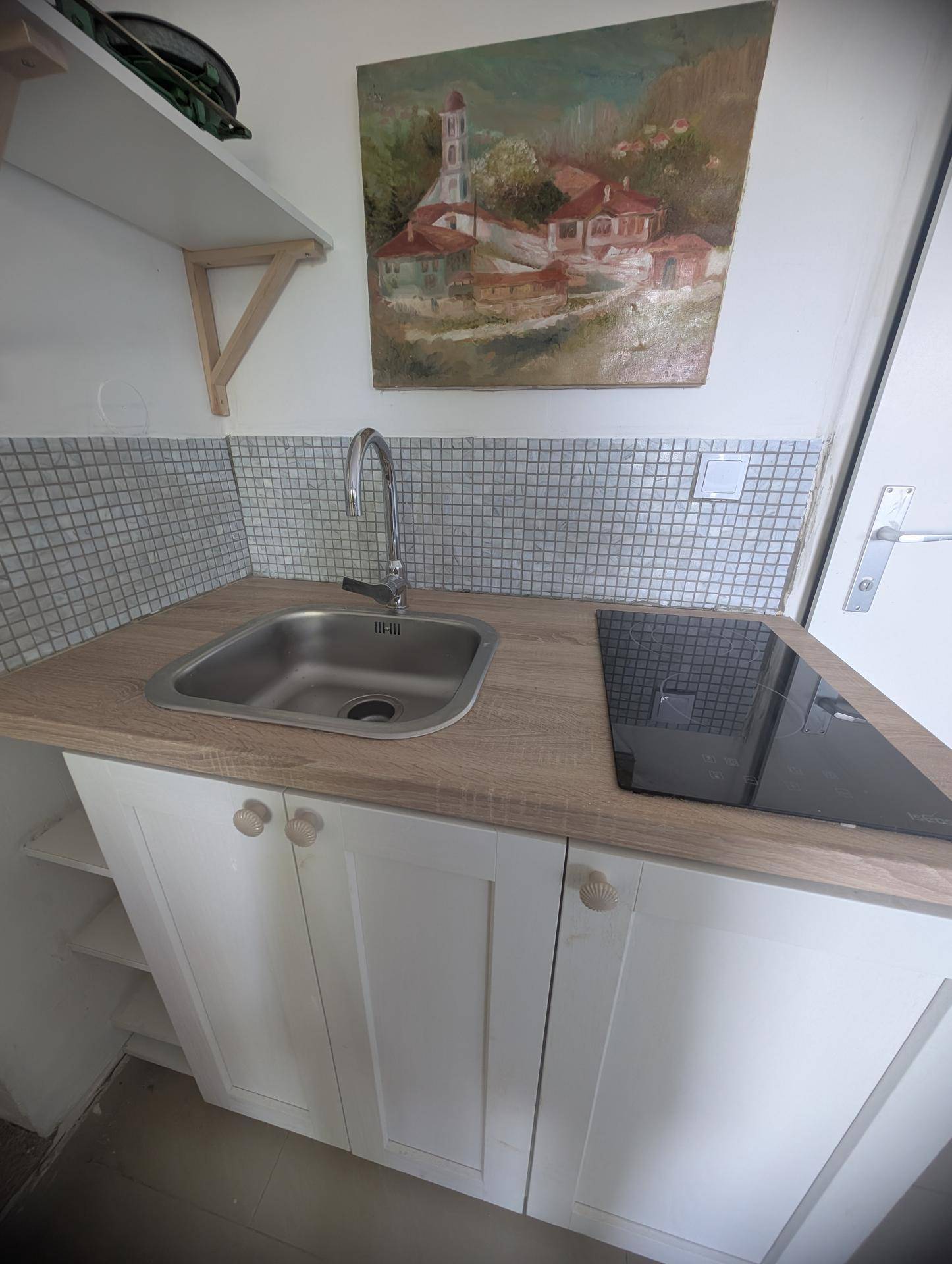 Kleine Küchenzeile mit Spüle, Induktionskochfeld und Mosaikfliesen als Spritzschutz.