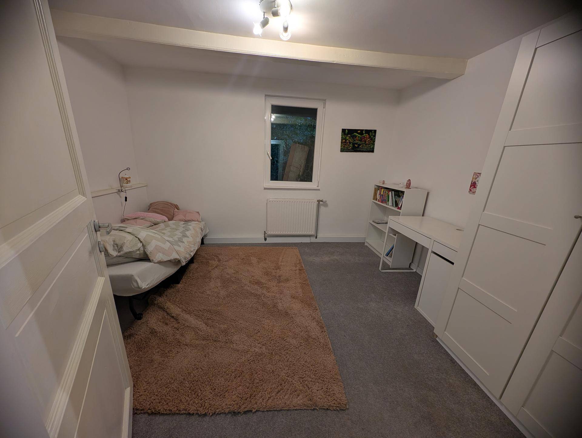 Gemütliches Schlafzimmer mit Teppichboden, weißem Kleiderschrank und Schreibtischbereich.