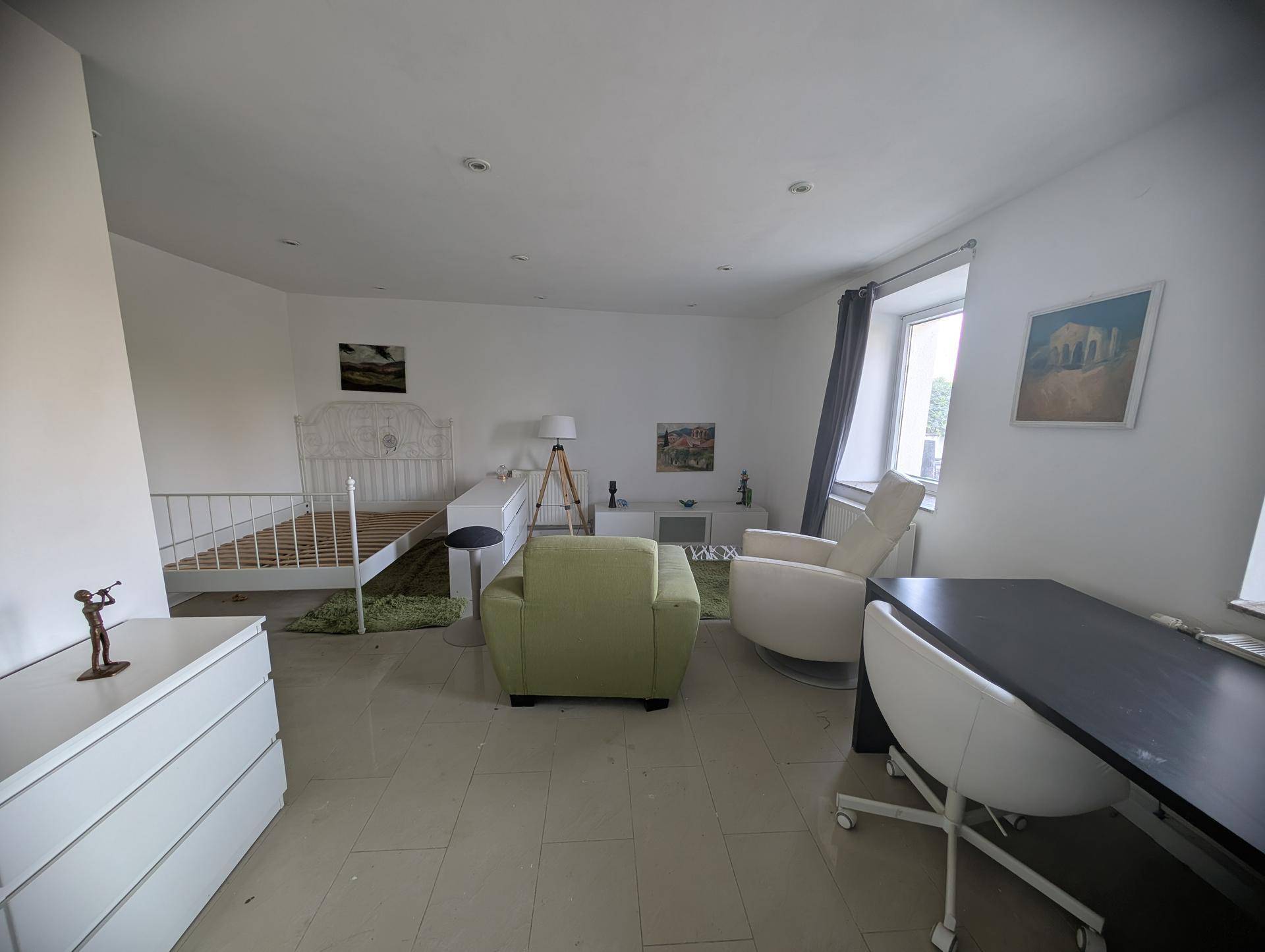 Helles Schlafzimmer mit Fliesenboden, weißem Bett und einem separaten Arbeitsbereich.