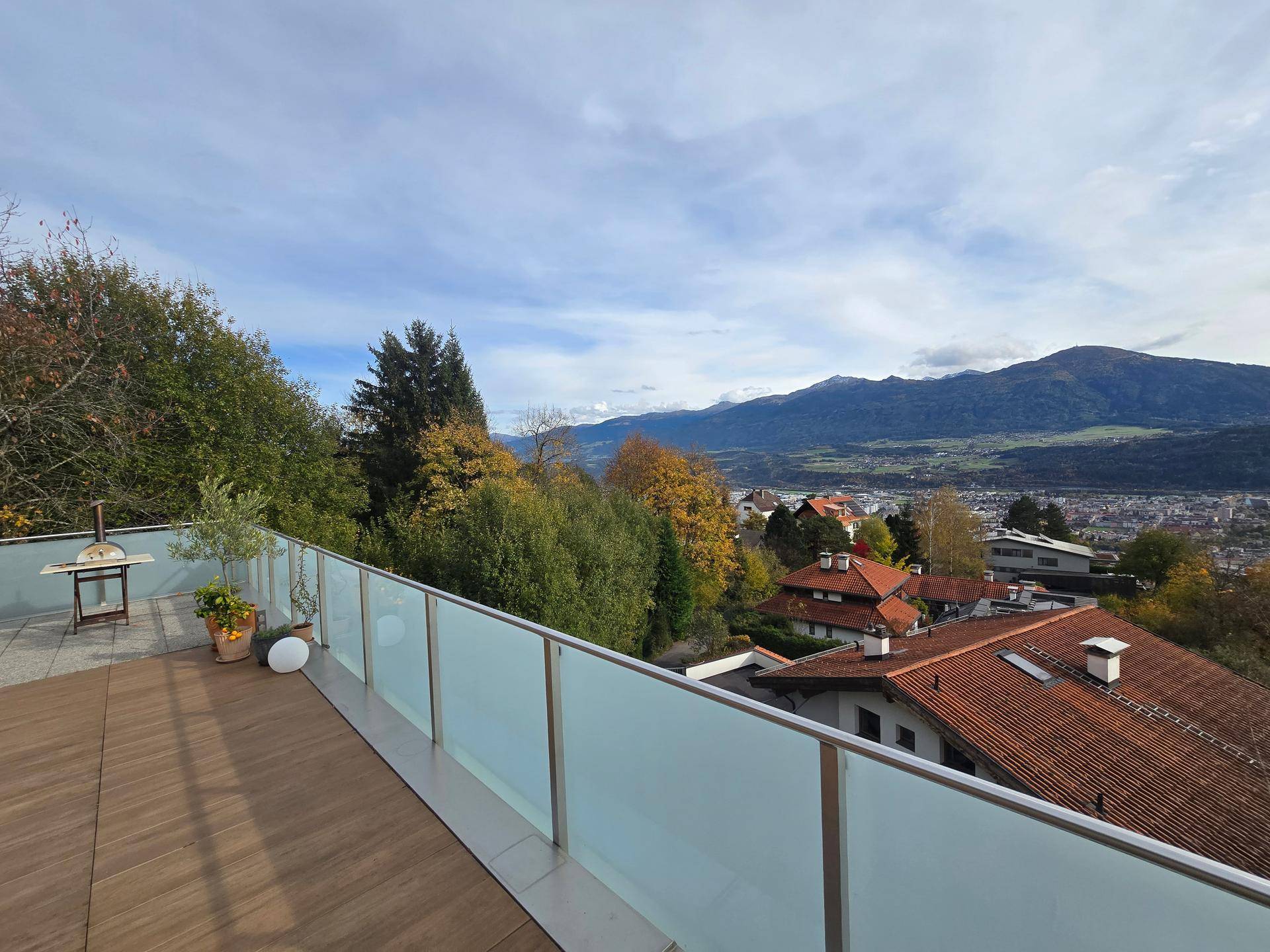 Terrasse mit Holzboden, Glasgeländer und Panoramablick auf die Stadt und die Berge.