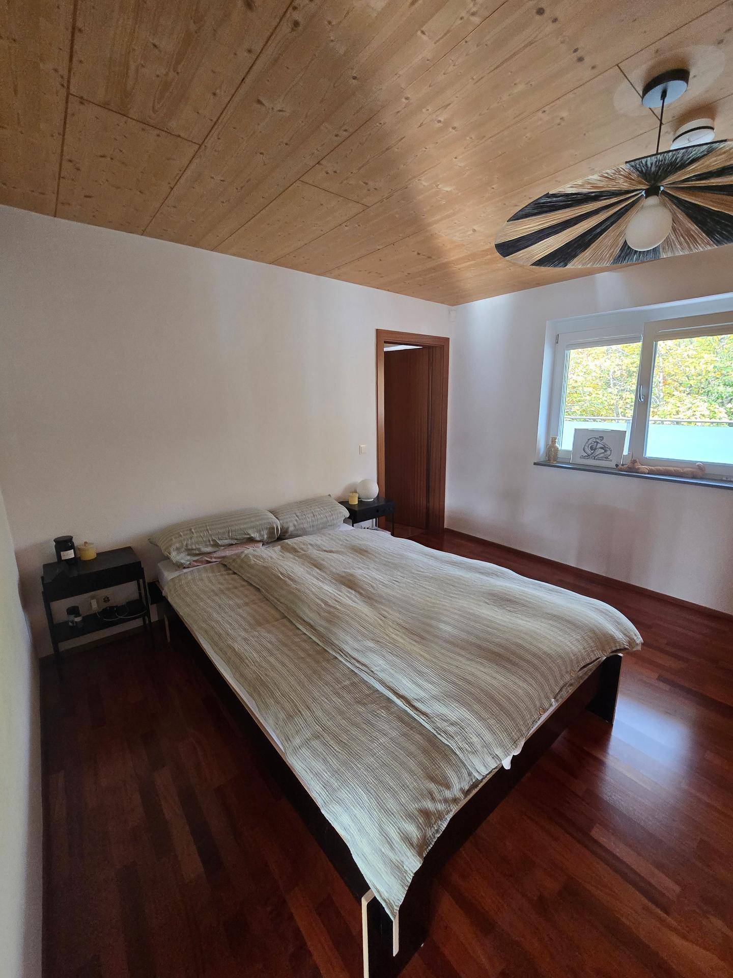 Gemütliches Schlafzimmer mit Holzboden, Holzbalkendecke und Fenster mit Blick ins Grüne.