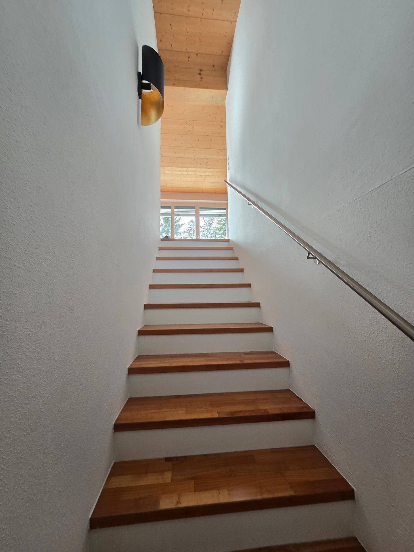 Holztreppe mit weiß gestrichenen Wänden und natürlichem Lichteinfall von oben.
