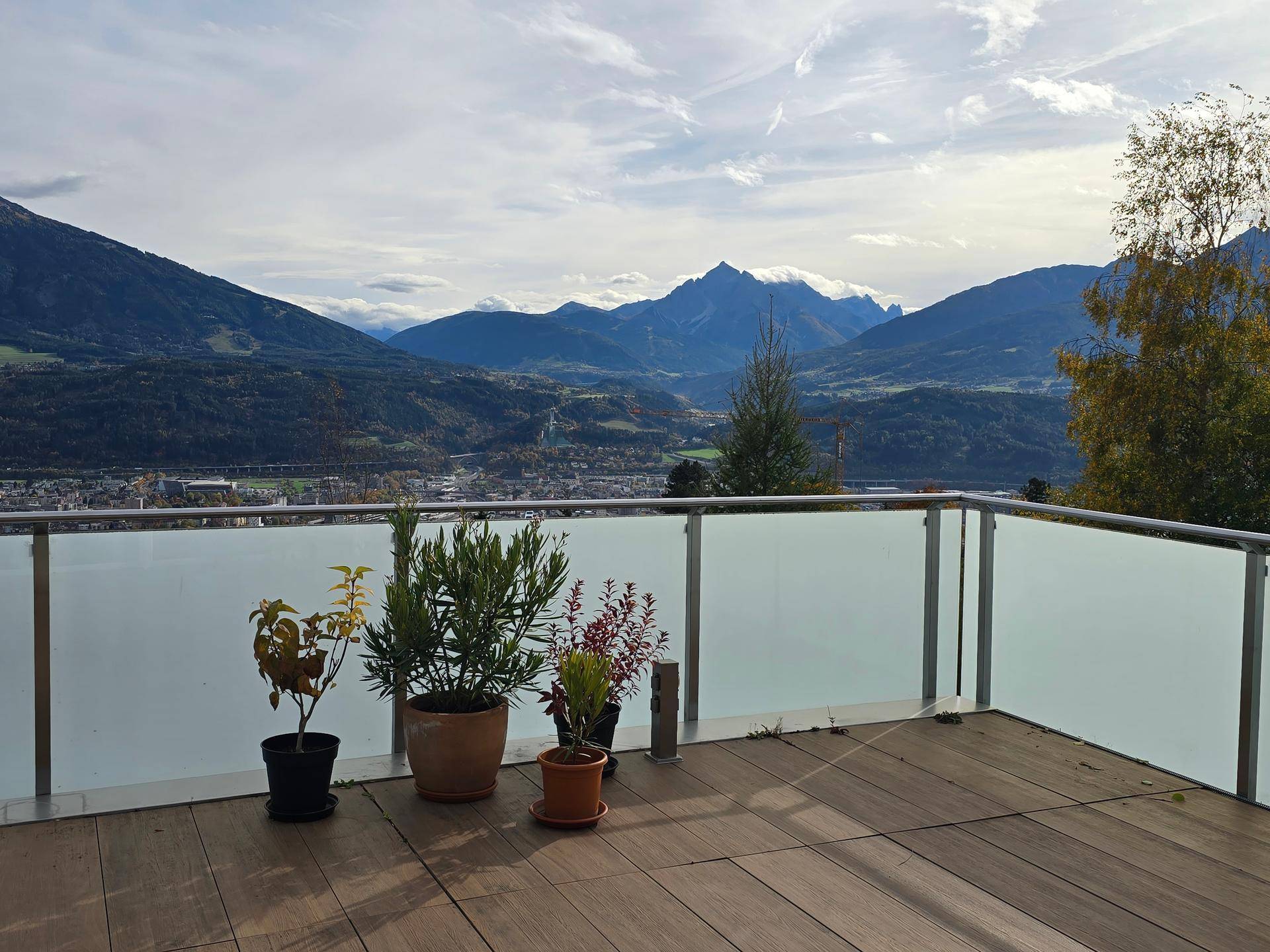 Sonniger Terrassenbereich mit Holzboden, Pflanzen und weitem Blick auf die Berge.