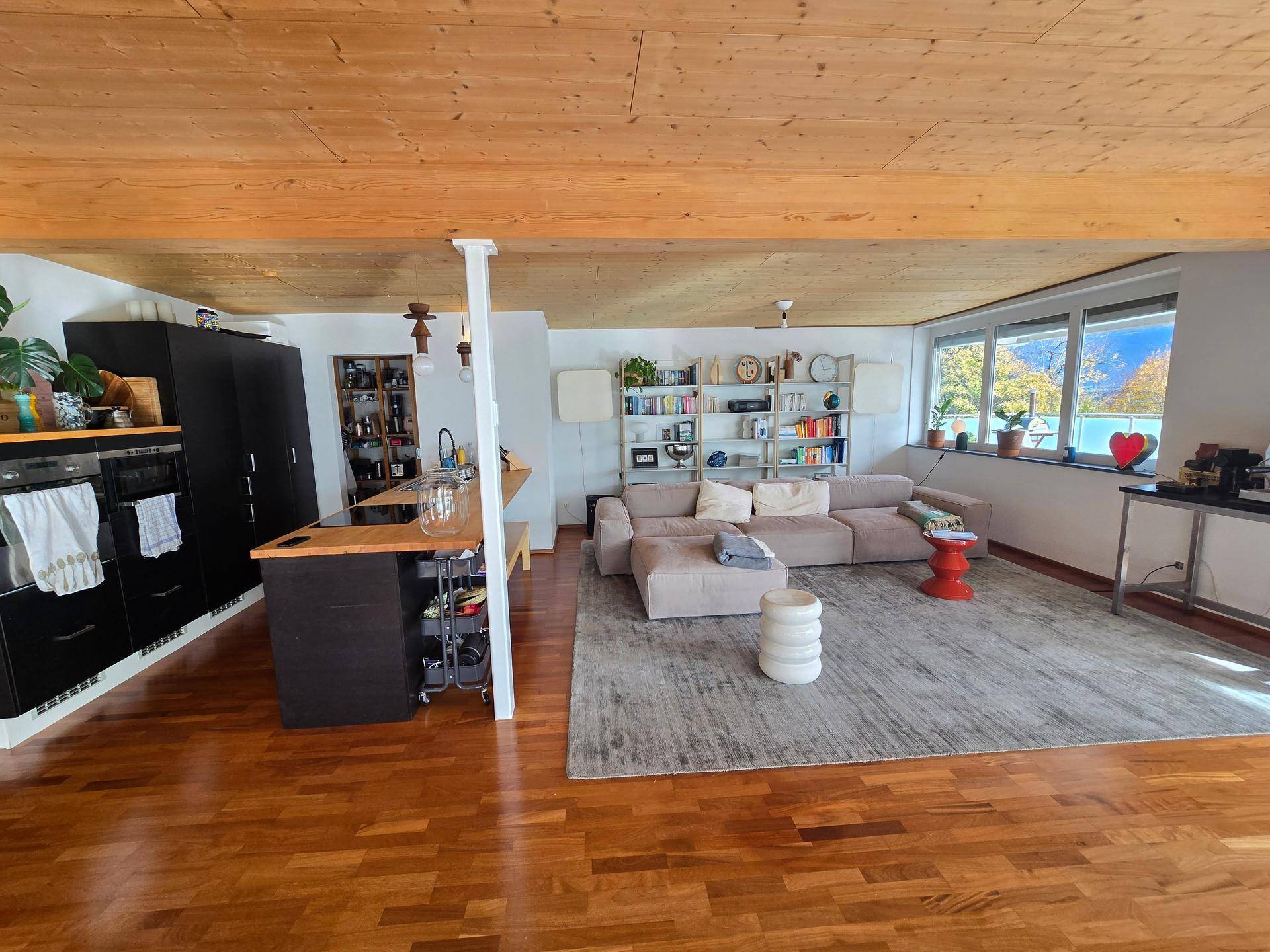 Offener Wohnbereich mit Holzbalkendecke, integrierter Küche und gemütlicher Sitzecke.