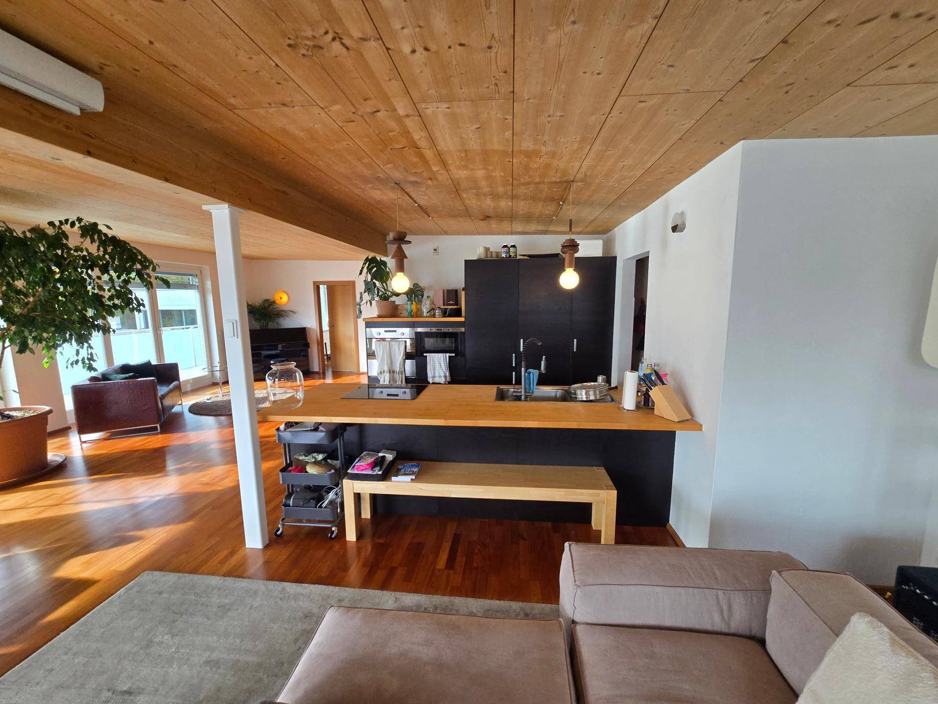 Offene Küche mit Holztheke, schwarzen Schränken und Holzbalkendecke im Wohnbereich.