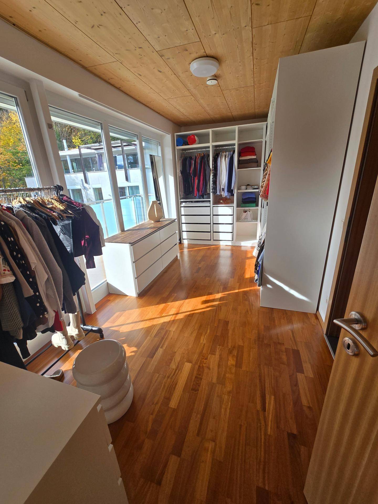 Helles Ankleidezimmer mit Holzboden, Einbauschränken und Zugang zu einem Balkon.