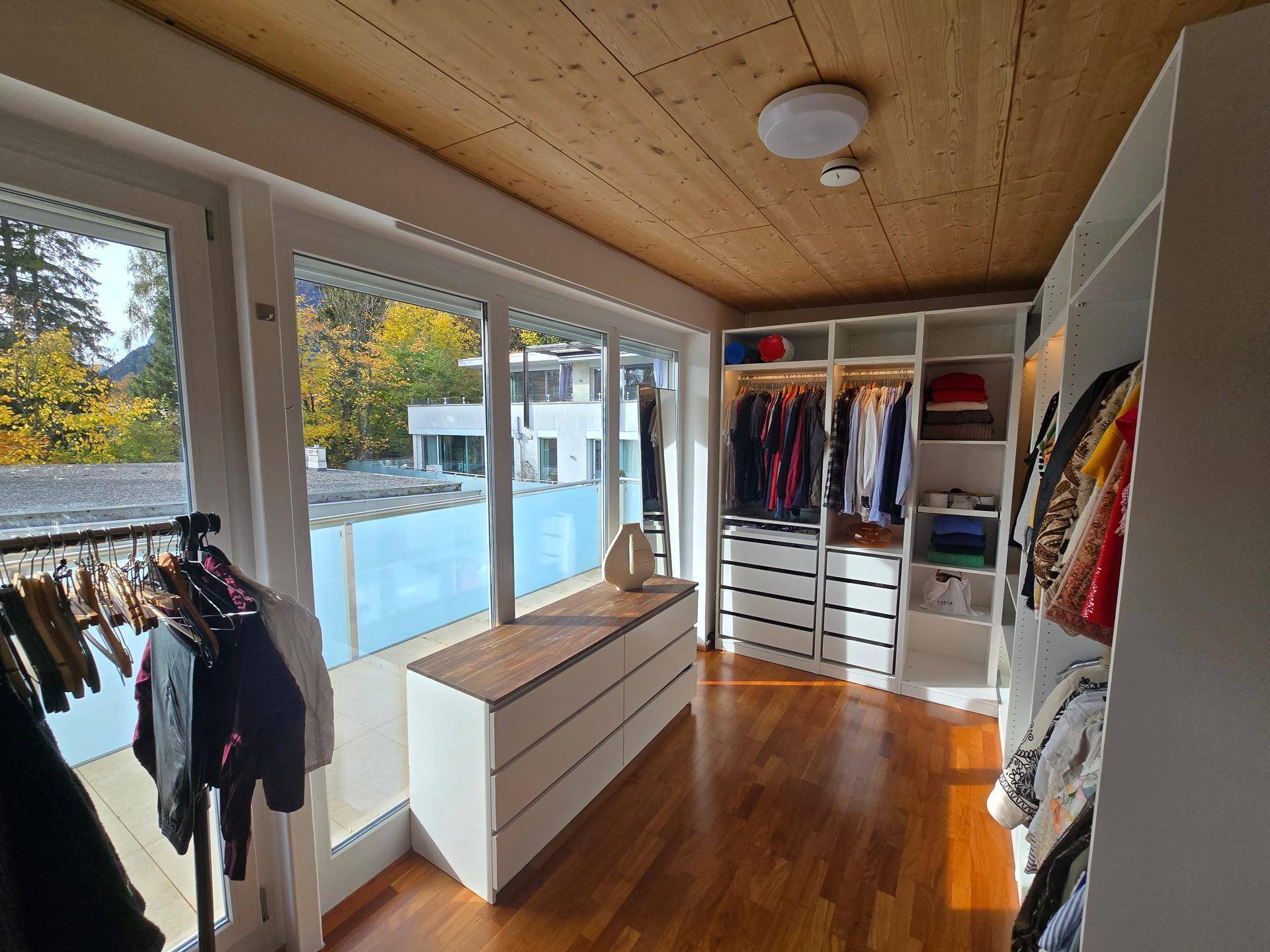 Helles Ankleidezimmer mit Einbauschränken, Holzboden und großem Fenster mit Balkonzugang.