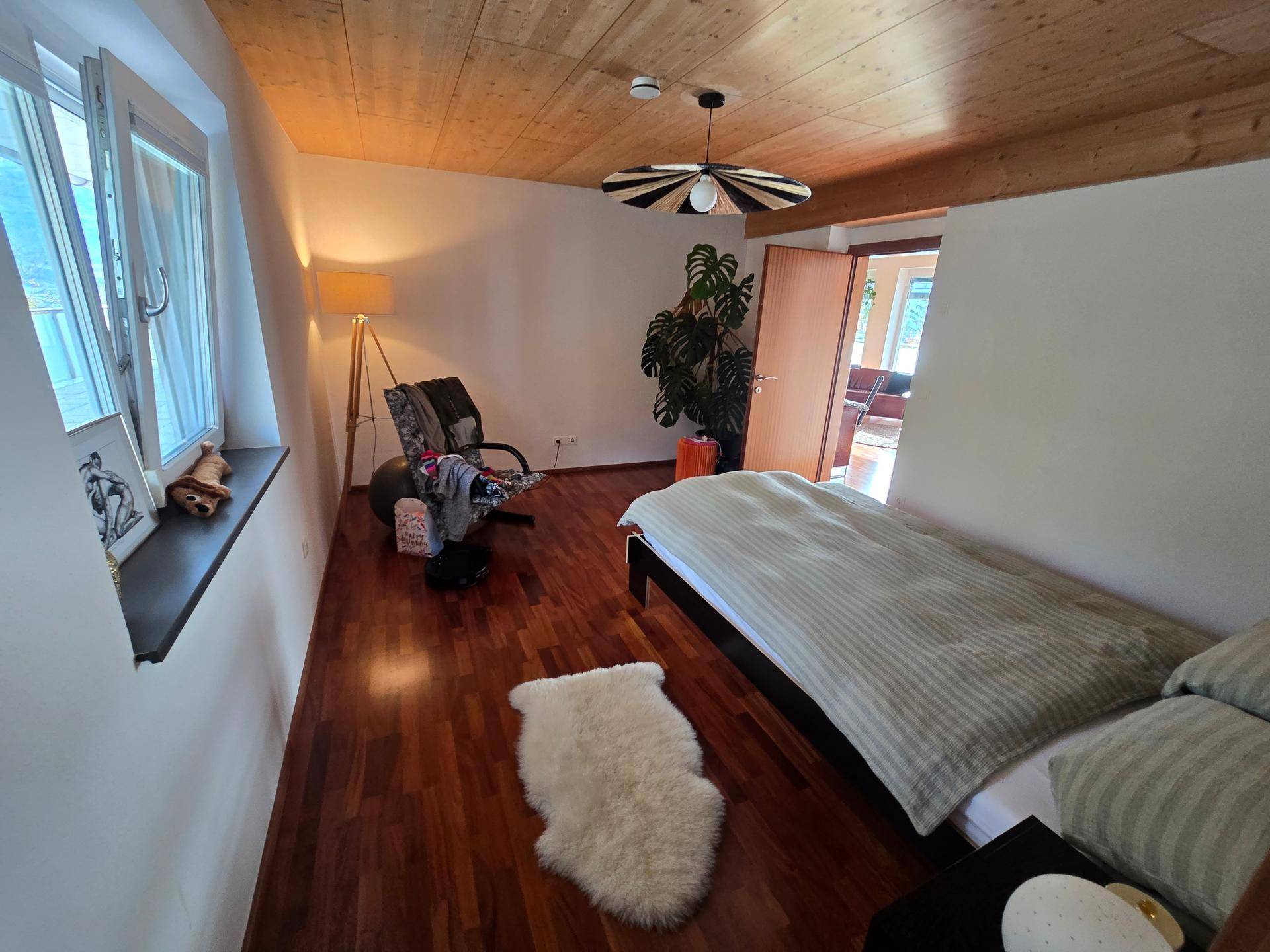 Schlafzimmer mit Holzboden, Holzbalkendecke und Fenster mit Blick auf die Umgebung.