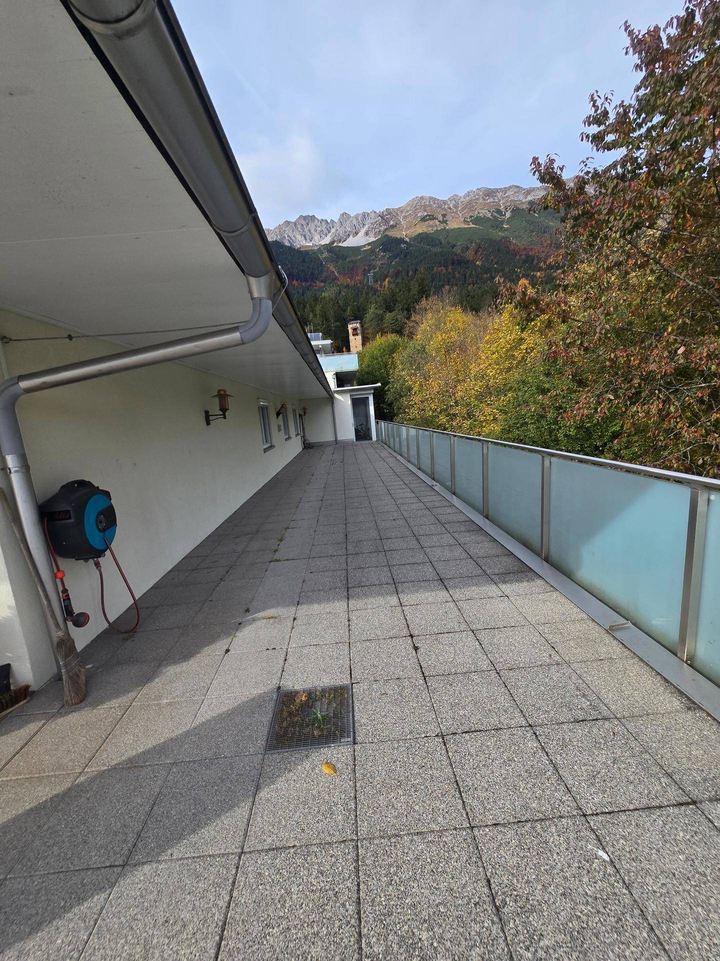 Langer, gefliester Terrassenbereich mit Bergblick und einem Gartenschlauch an der Wand.