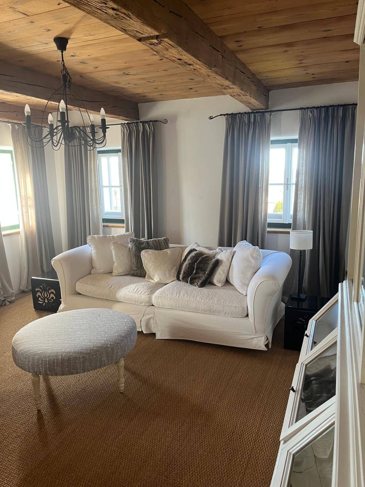 Heller Wohnbereich mit beigem Teppichboden, weißem Sofa und Holzbalkendecke für ein warmes Ambiente.