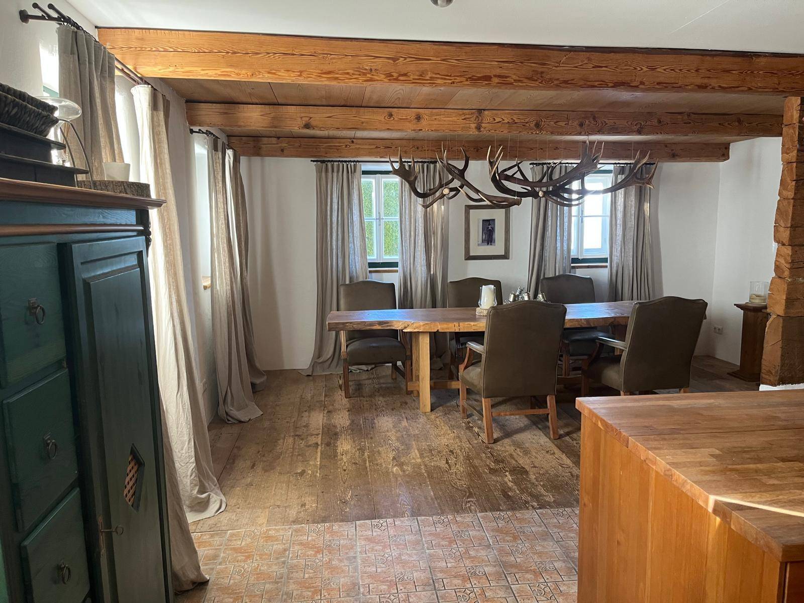 Geräumiger Essbereich mit Holzbalkendecke, großem Holztisch und einem beeindruckenden Hirschgeweih-Kronleuchter.