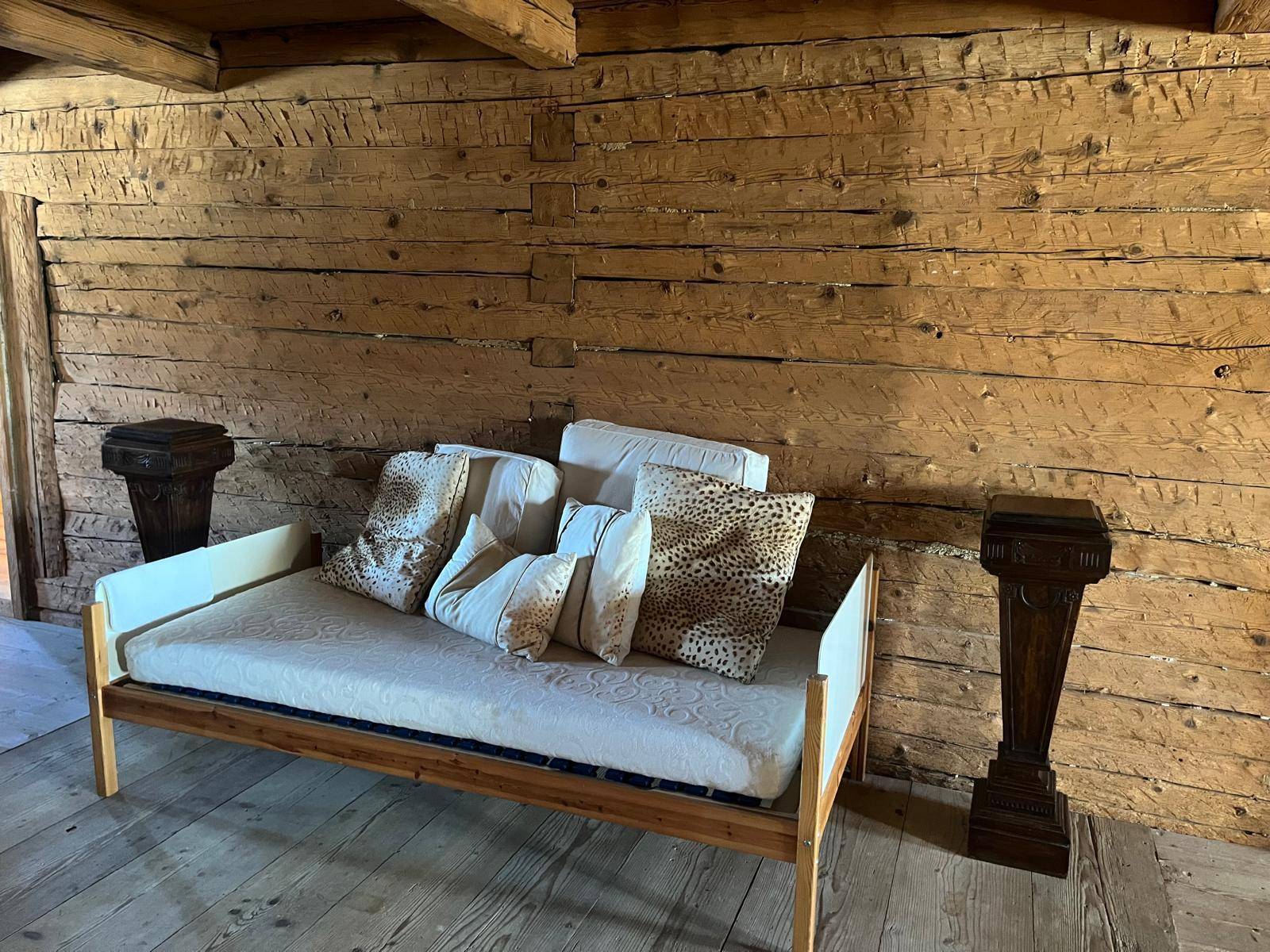 Rustikaler Raum mit Holzwänden, Holzboden und einem einfachen Tagesbett für Gäste oder Entspannung.