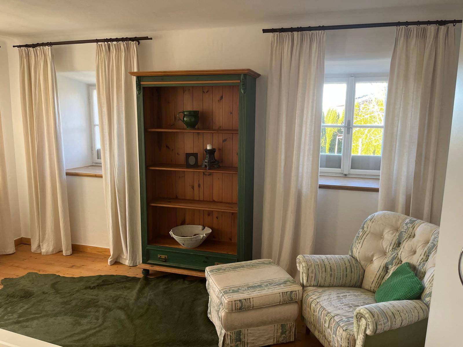 Heller Raum mit Holzboden, Bücherregal und einem bequemen Sessel am Fenster für Lesestunden.