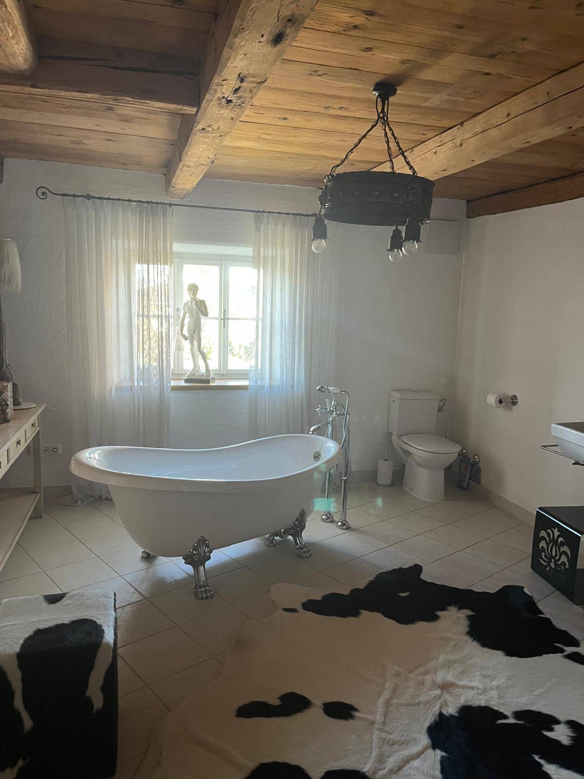 Geräumiges Badezimmer mit freistehender Badewanne, Fliesenboden und viel Tageslicht durch das Fenster.