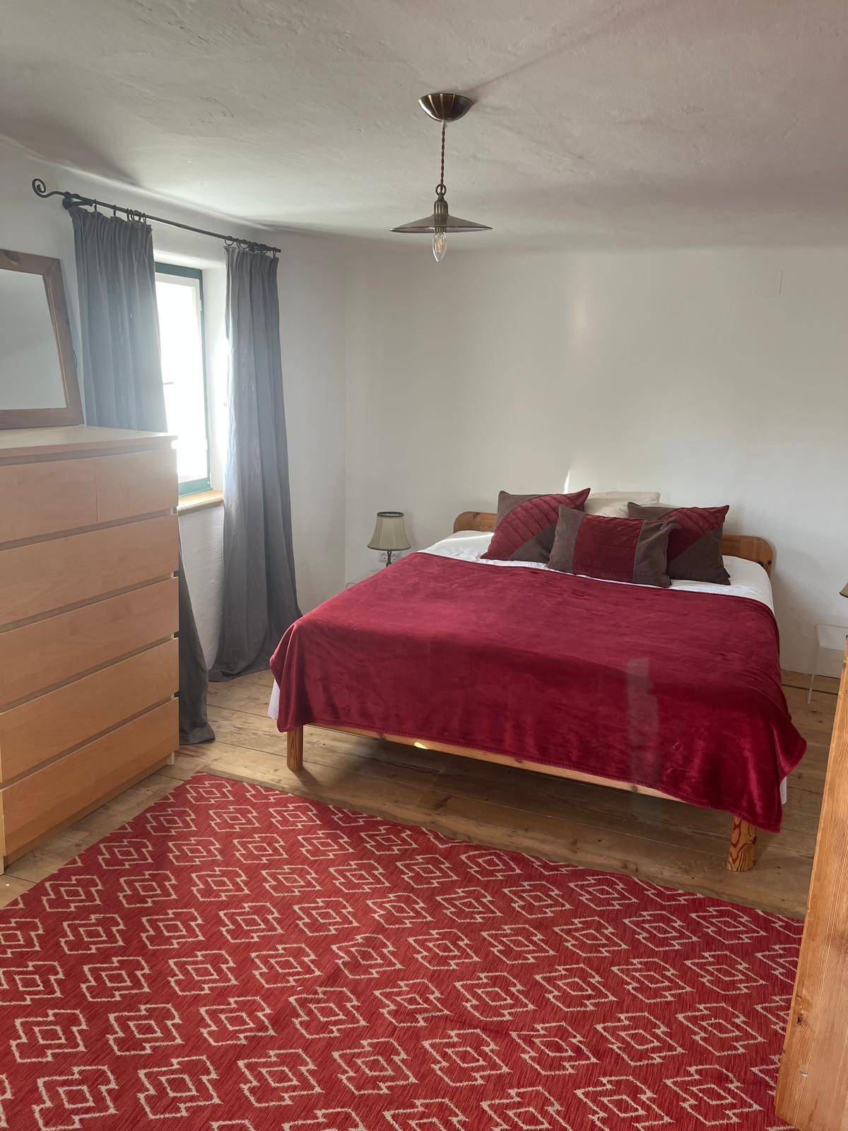 Helles Schlafzimmer mit Holzboden, rotem Teppich und einfacher, gemütlicher Einrichtung.