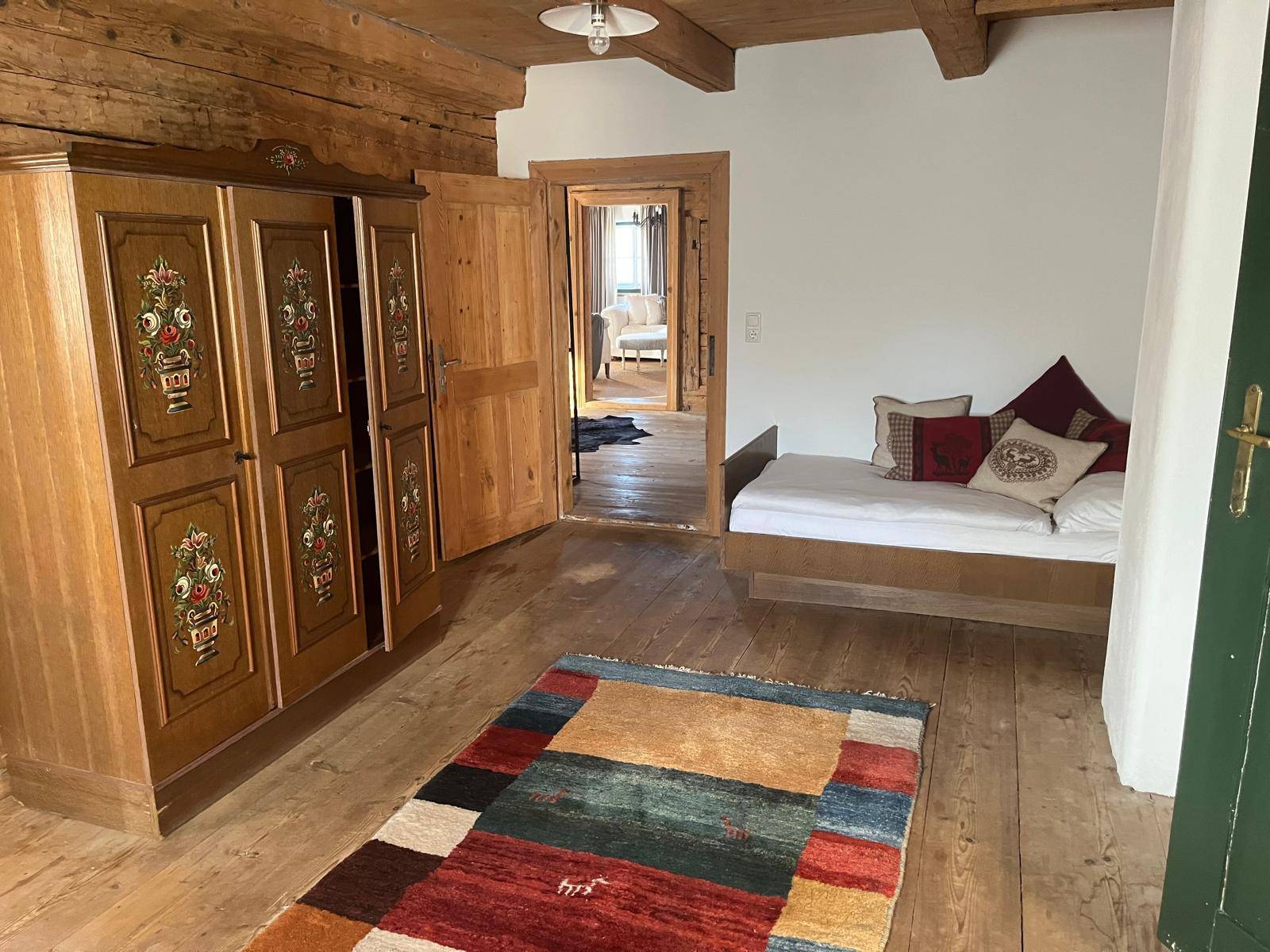 Schlafzimmer mit Holzboden, traditionellem Kleiderschrank und farbenfrohem Teppich für Gemütlichkeit.