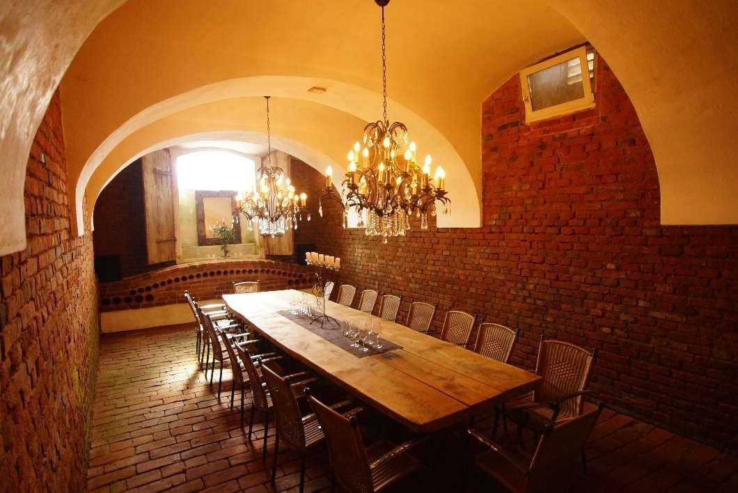 Historischer Gewölbekeller mit langer Holztafel, Ziegelwänden und opulenten Kronleuchtern für Feierlichkeiten.