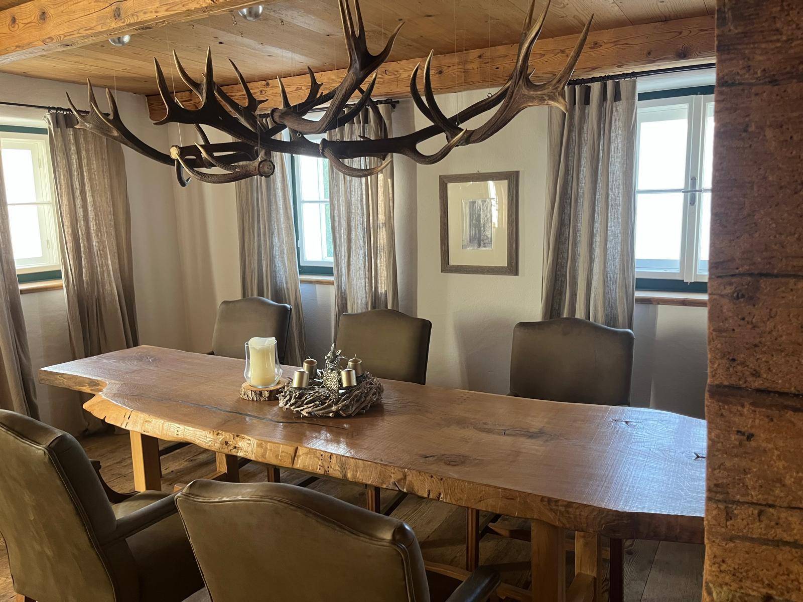 Esszimmer mit großem Holztisch, Hirschgeweih-Kronleuchter und Holzbalkendecke für rustikalen Charme.