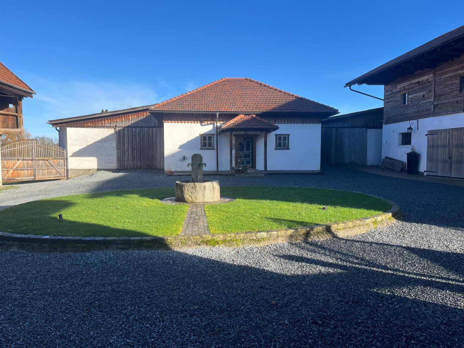 Weitläufiges ländliches Anwesen mit mehreren Gebäuden, Kiesfläche und einem zentralen Brunnen.