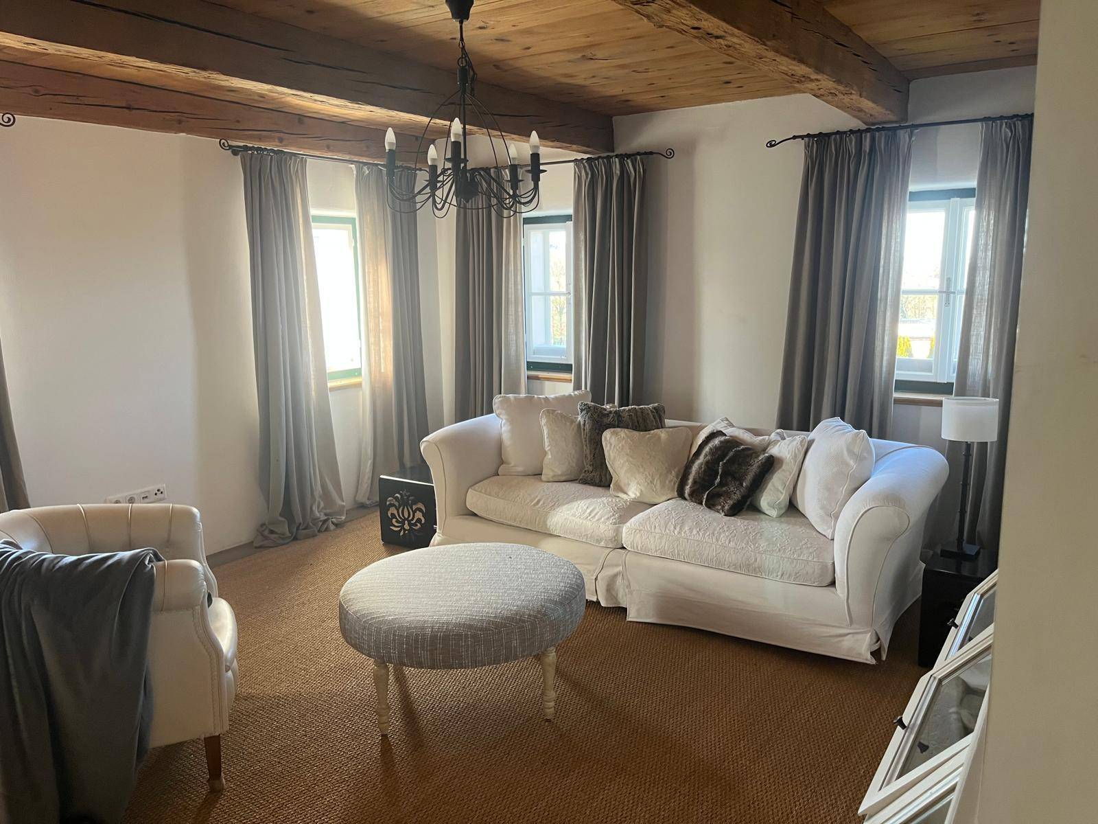 Gemütliches Wohnzimmer mit Holzbalkendecke, hellem Sofa und natürlichem Lichteinfall durch die Fenster.