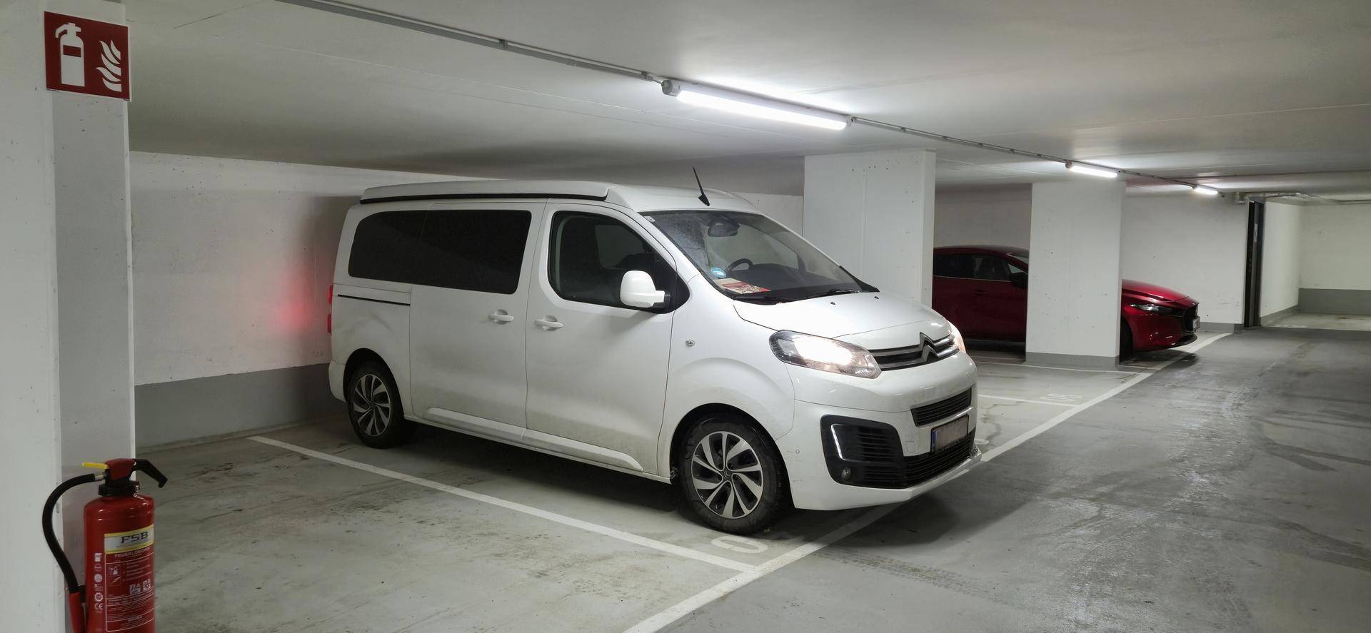 Weißer Van auf einem Stellplatz in der Tiefgarage mit einem roten Feuerlöscher in der Nähe.