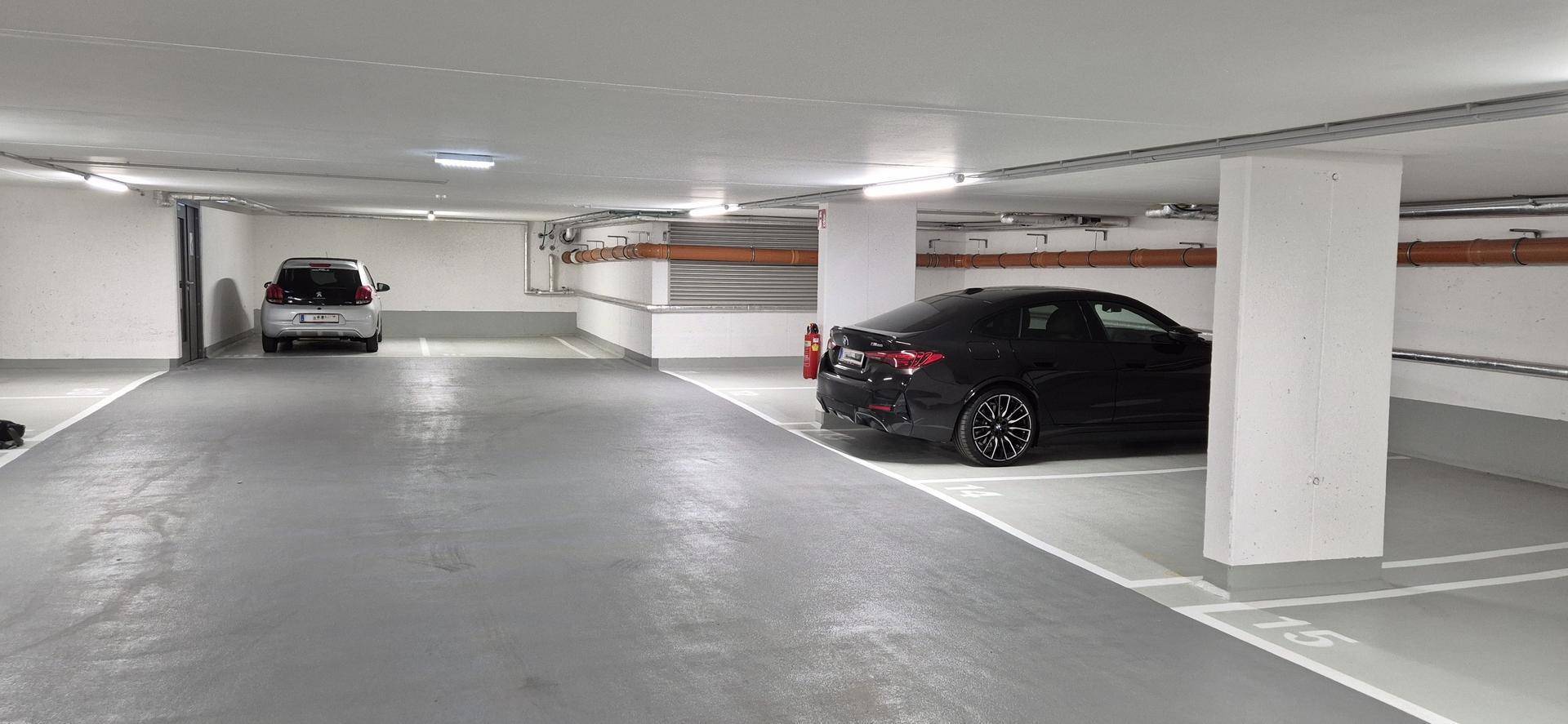 Geräumige Tiefgarage mit einem schwarzen und einem weißen Auto auf markierten Stellplätzen.